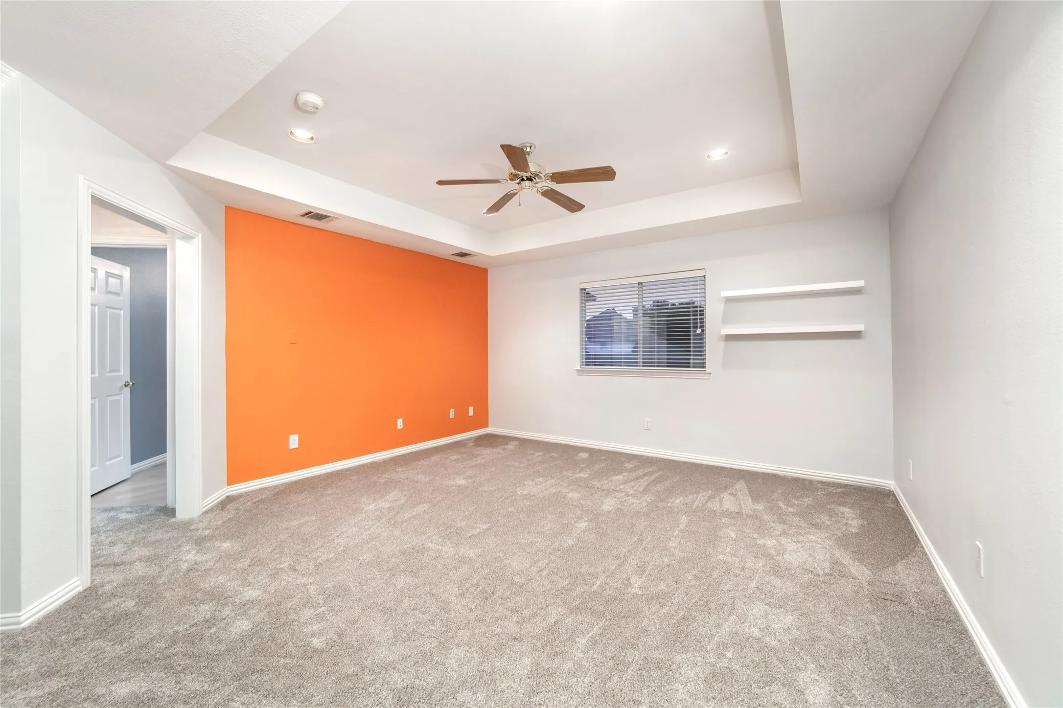 Spacious interior room featuring a tray ceiling with a ceiling fan, recessed lighting, and a vibrant accent wall