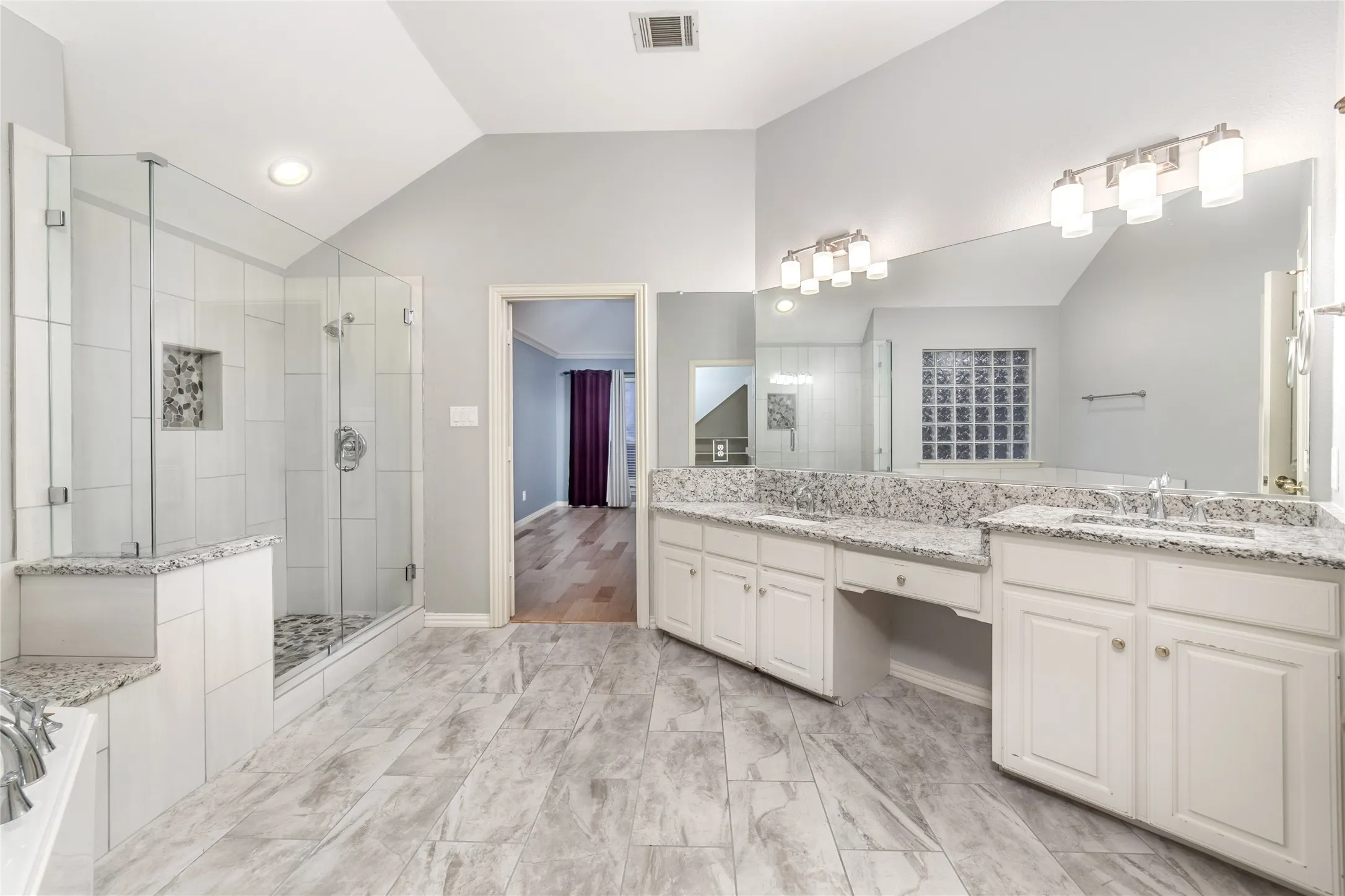 Spacious bathroom featuring dual vanities with light-colored countertops, a large frameless glass shower enclosure, and grey-toned tile flooring