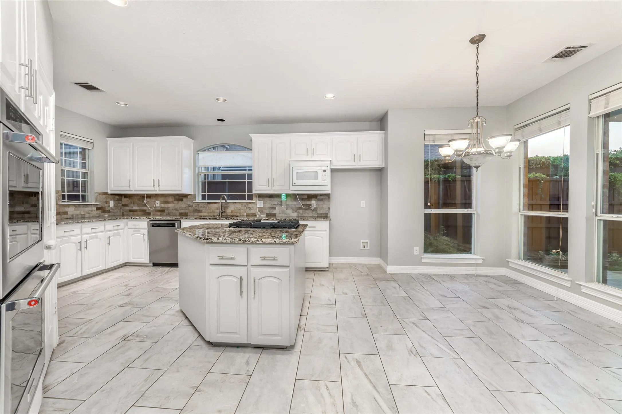 Kitchen featuring white cabinetry, a central island with a cooktop, stone countertops, and a tile backsplash