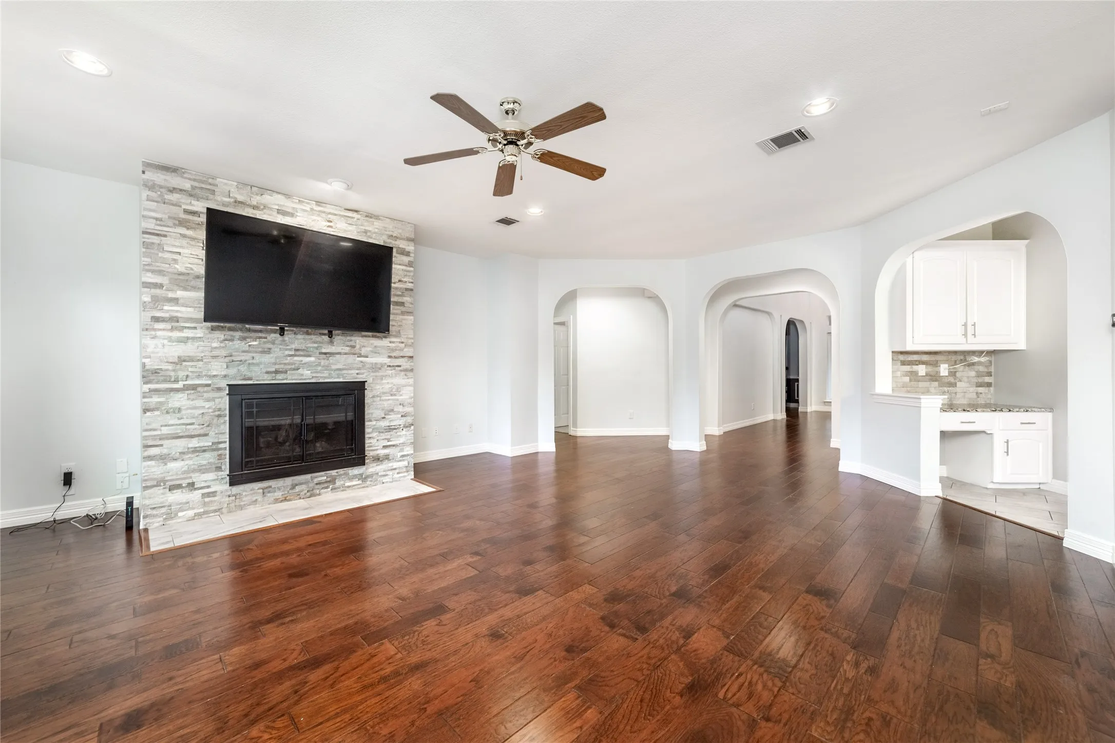 Spacious living area featuring wood-finish flooring, a stone-clad fireplace, and a ceiling fan