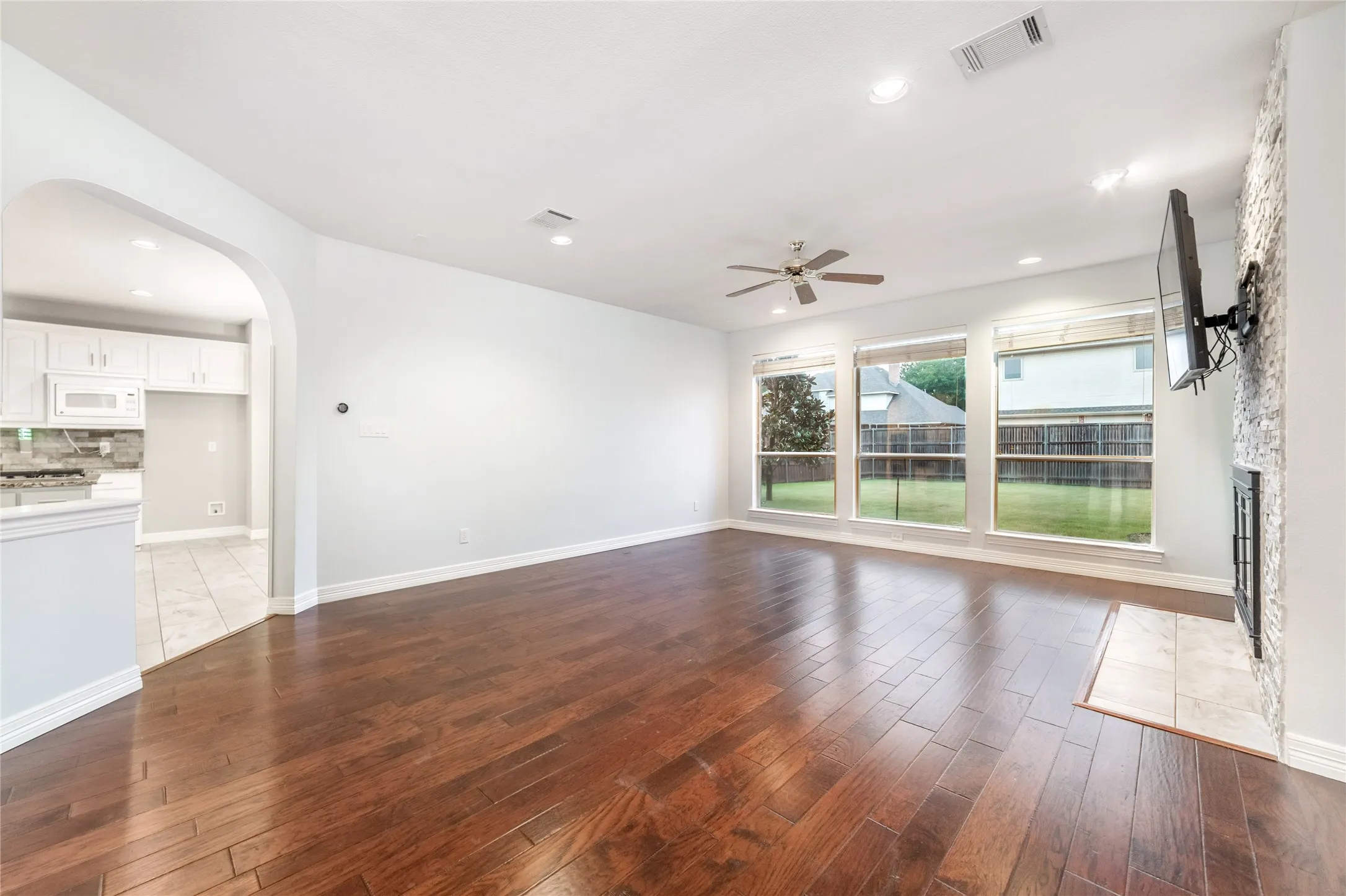 Spacious living area featuring rich wood-finish flooring, a stone-clad fireplace, and a ceiling fan