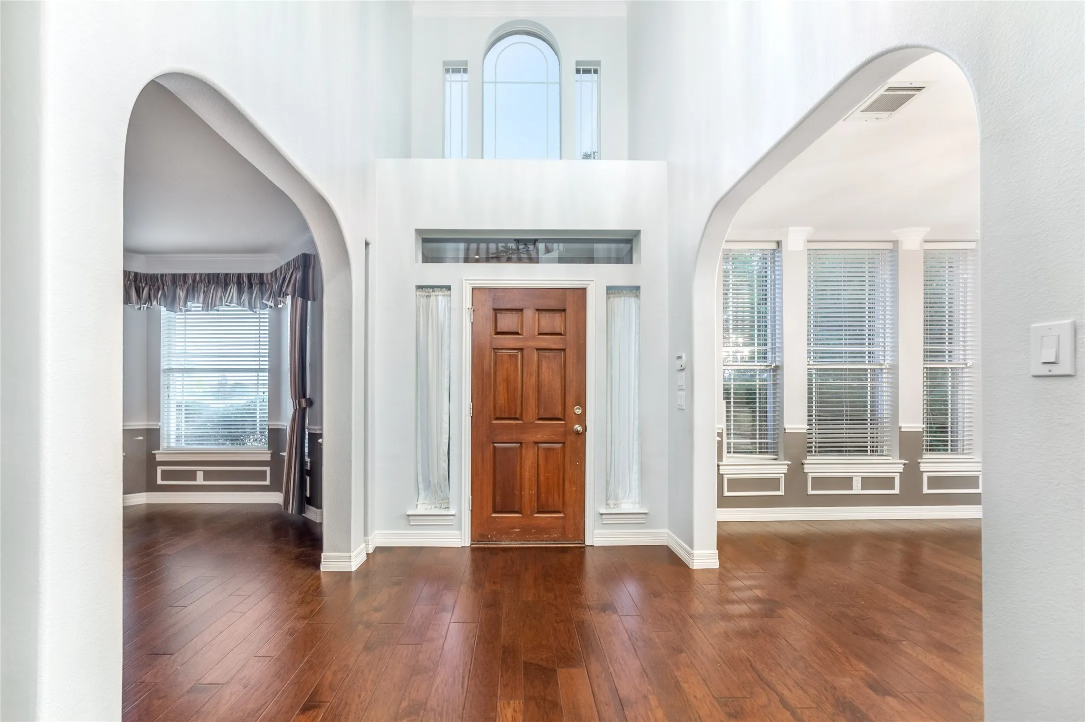 Two-story foyer featuring a paneled wood-finish entry door with transom and sidelight windows, arched doorways, and wood-finish flooring
