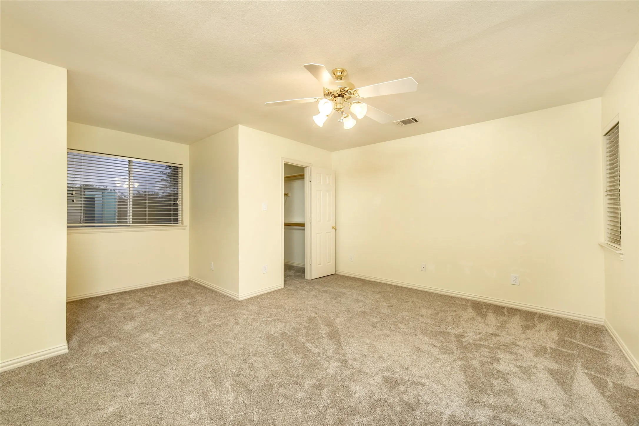 Carpeted room with a ceiling fan light fixture, two windows with blinds, and a built-in closet with shelving