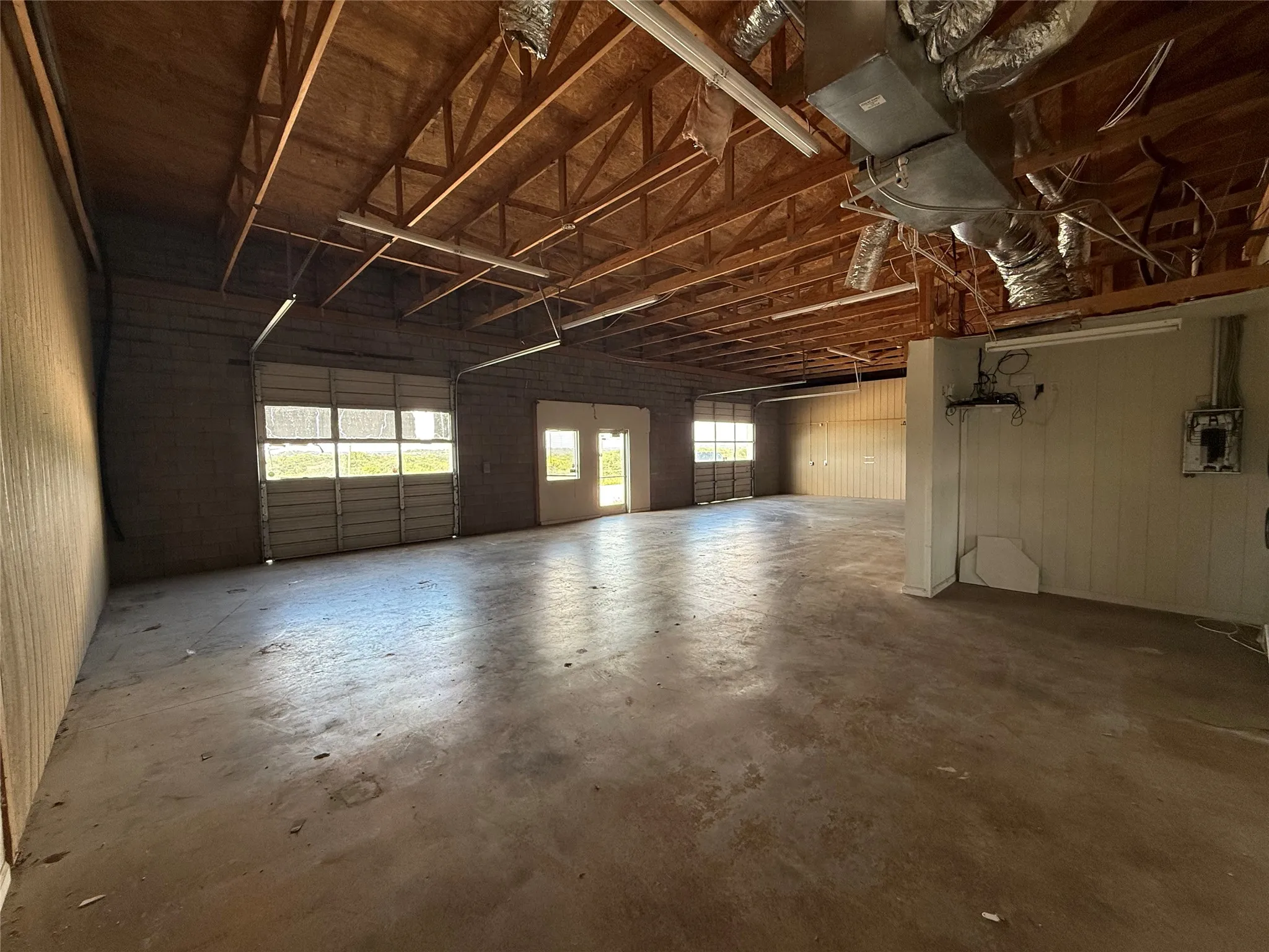 Expansive open-concept interior featuring a concrete floor, exposed wood beam ceiling, and two overhead garage doors