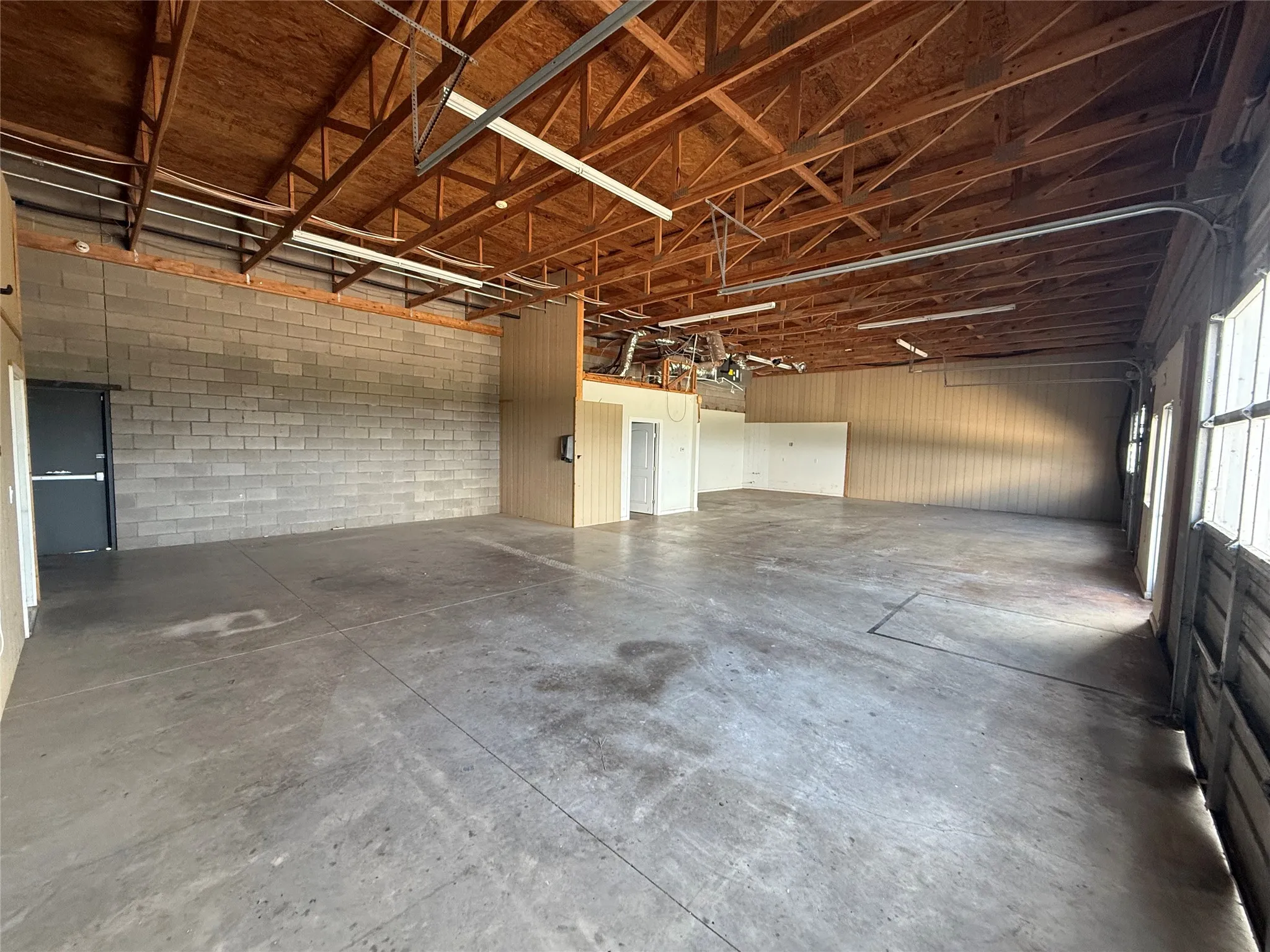 Expansive interior space featuring exposed wood beam ceilings, concrete block walls, and concrete flooring