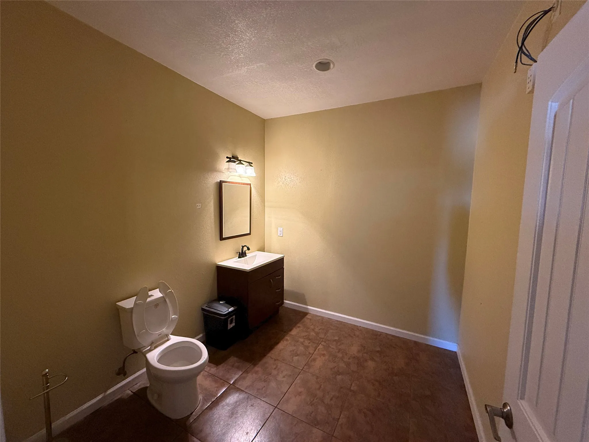 Bathroom featuring a brown-toned tile floor, a dark wood-finish vanity with an integrated sink, a rectangular framed mirror, and a three-light fixture