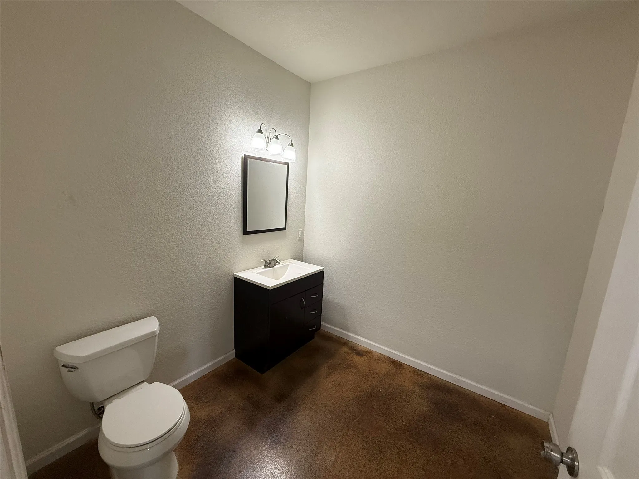 Powder room featuring a dark wood-finish vanity with an integrated white sink, a rectangular mirror, and a three-light vanity fixture