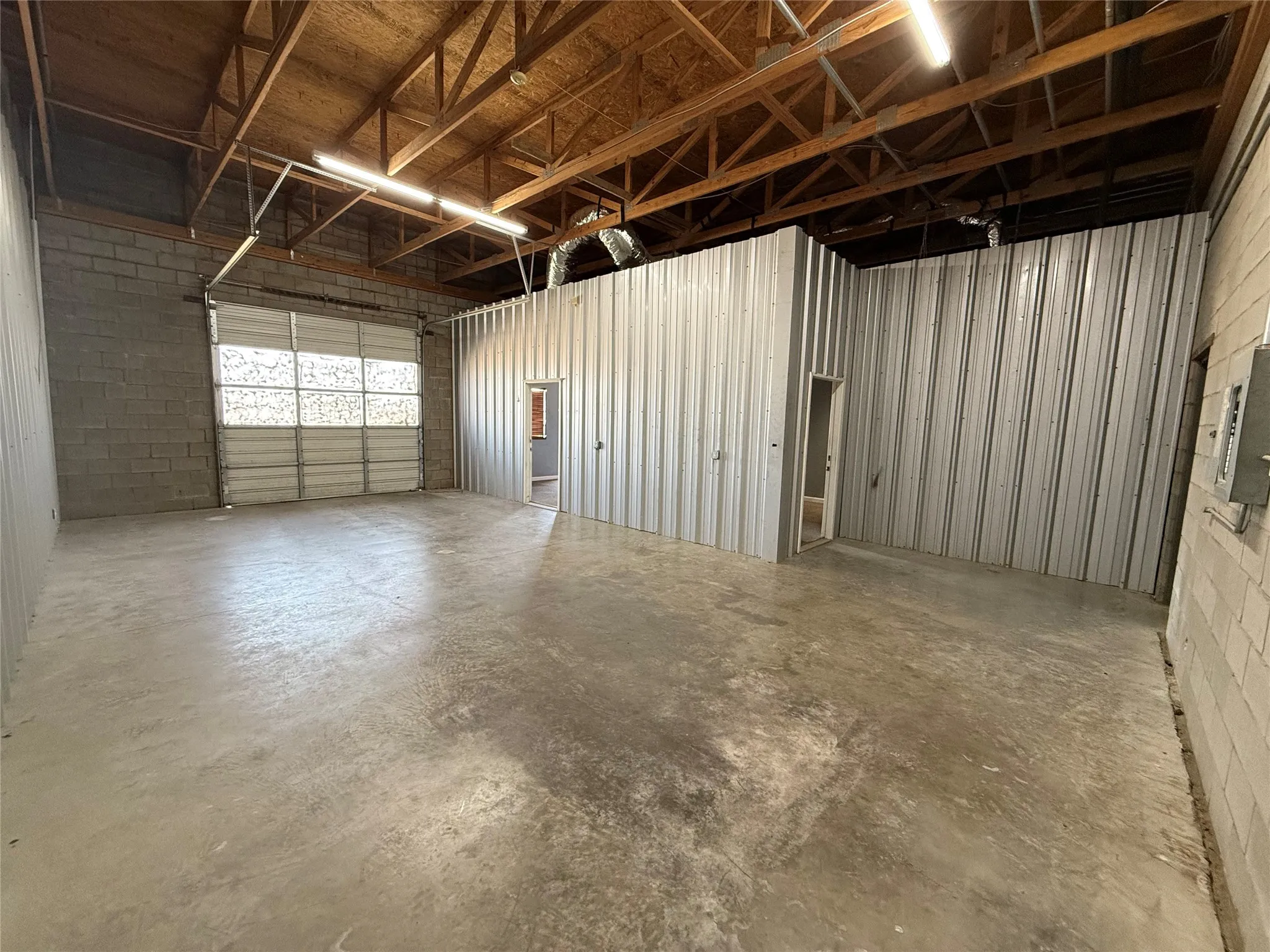 Spacious interior featuring a concrete floor, exposed wood ceiling trusses, and a large roll-up door