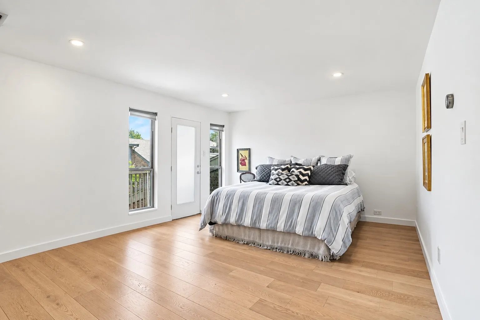 Light wood-finish flooring, recessed ceiling lighting, a door with frosted glass, and two windows with roller shades