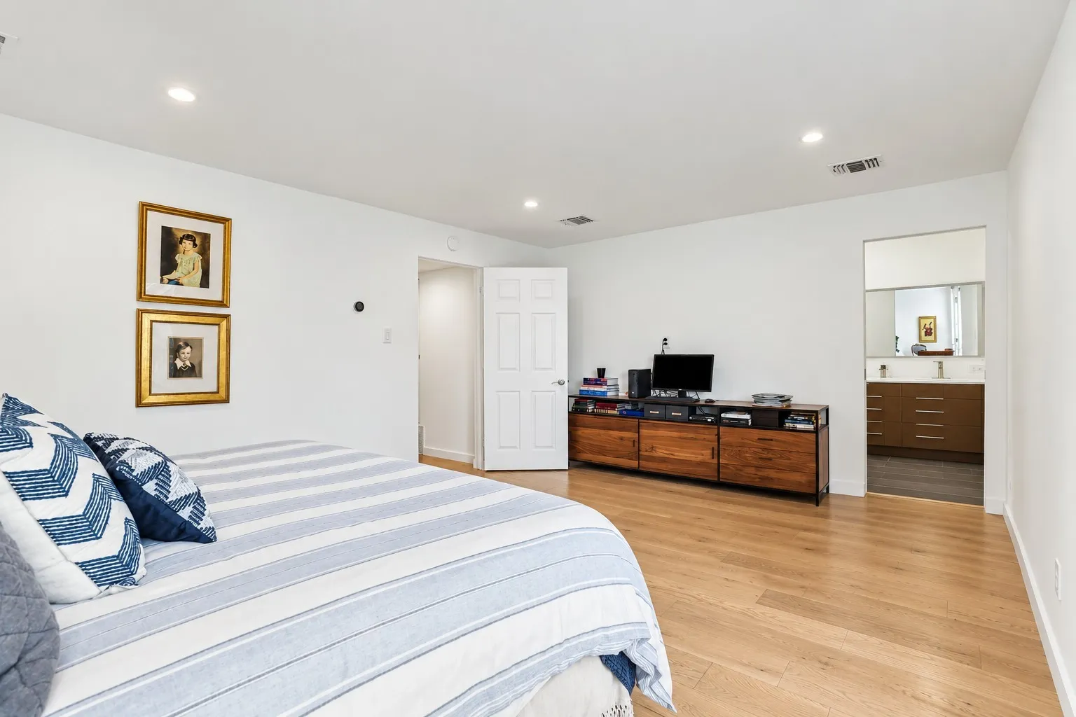 Recessed lighting, wood-finish flooring, white walls, and a visible vanity with dual vessel sinks