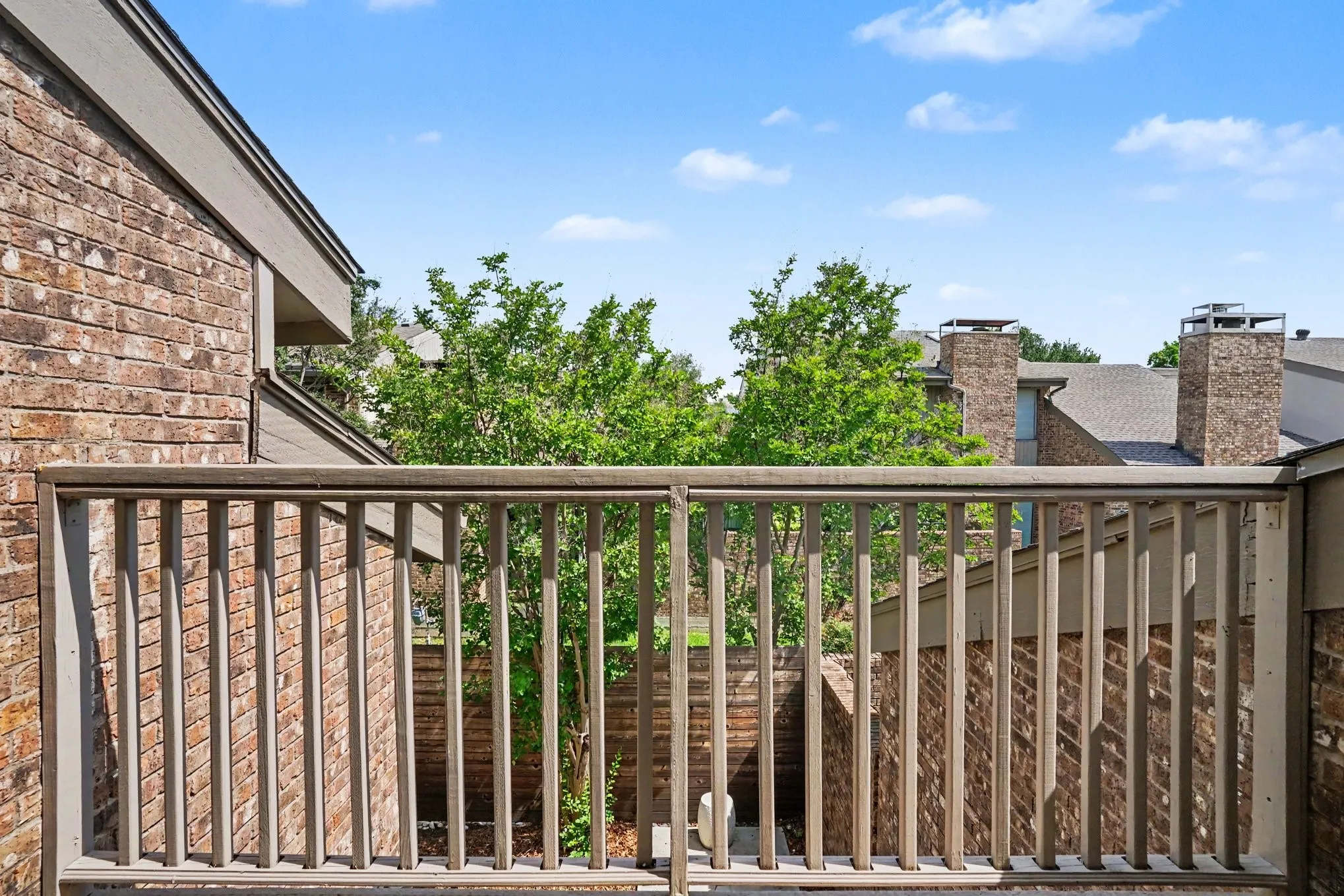 Exterior balcony featuring a wood-tone railing and brick facade