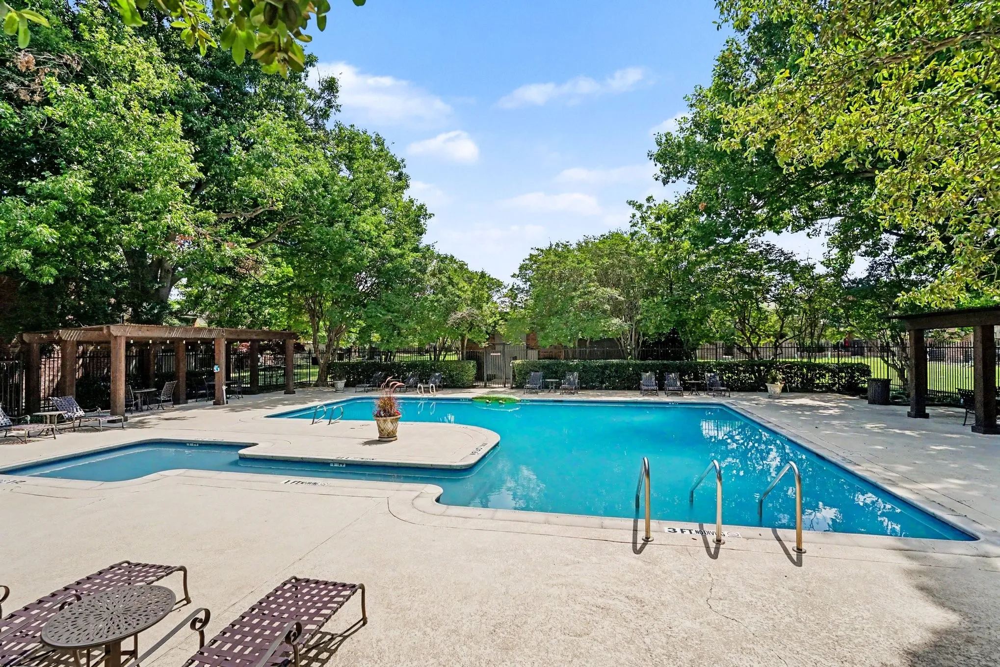 Expansive swimming pool area featuring a large main pool, an attached wading pool, and surrounding concrete decking