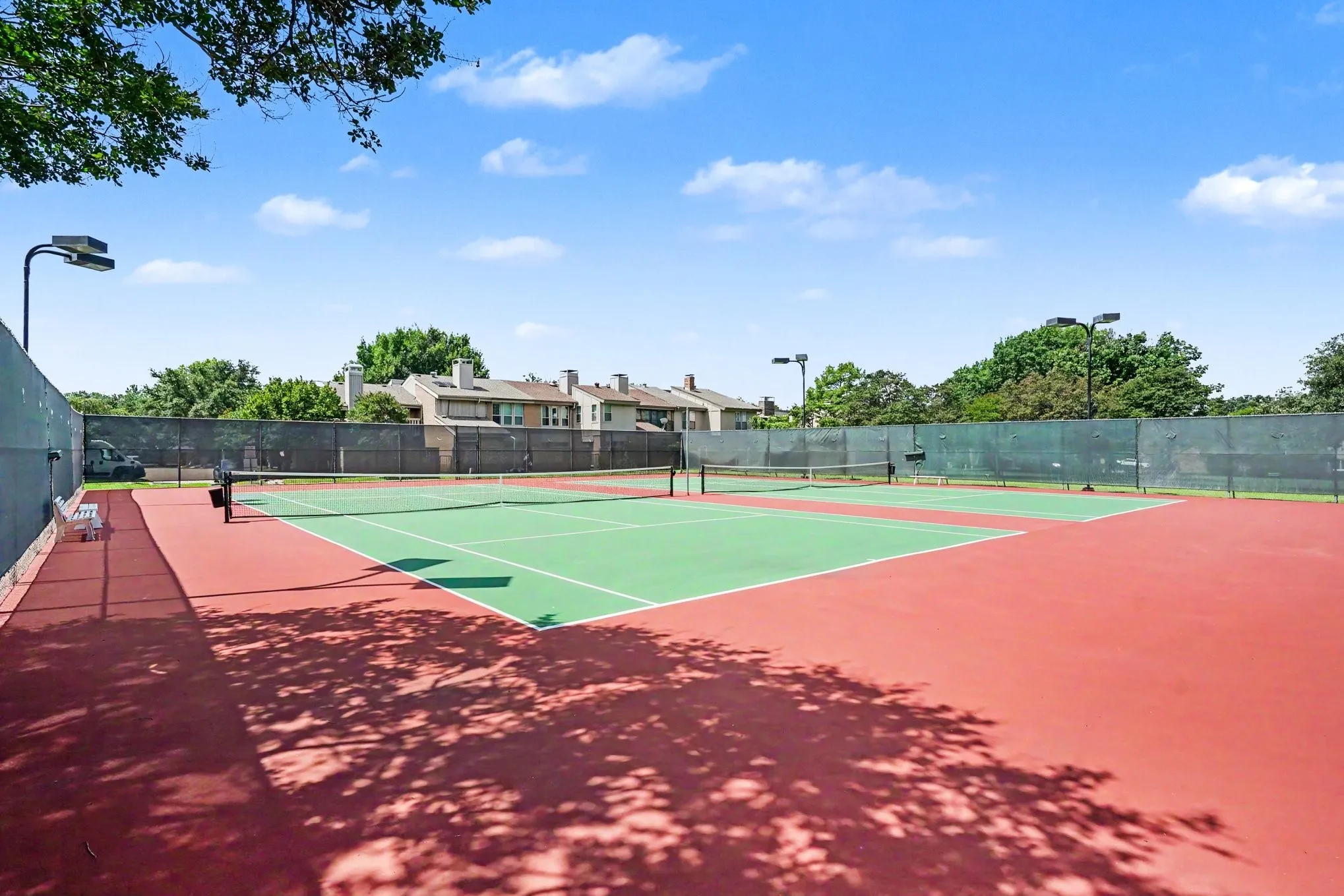 Dual hard-surface tennis courts featuring green playing areas and red surrounds