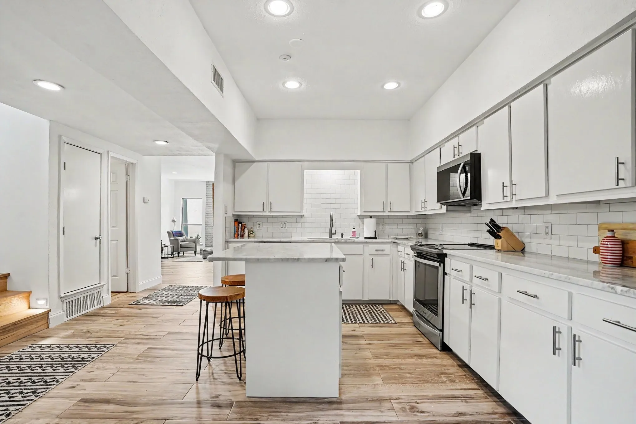 Open-concept kitchen featuring wood-finish flooring, white cabinetry, subway tile backsplash, and an island with a light-toned countertop