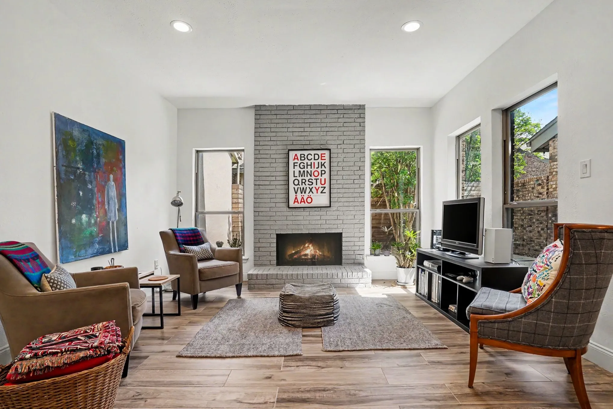 Living area featuring a painted brick fireplace, wood-finish flooring, recessed lighting, and multiple windows