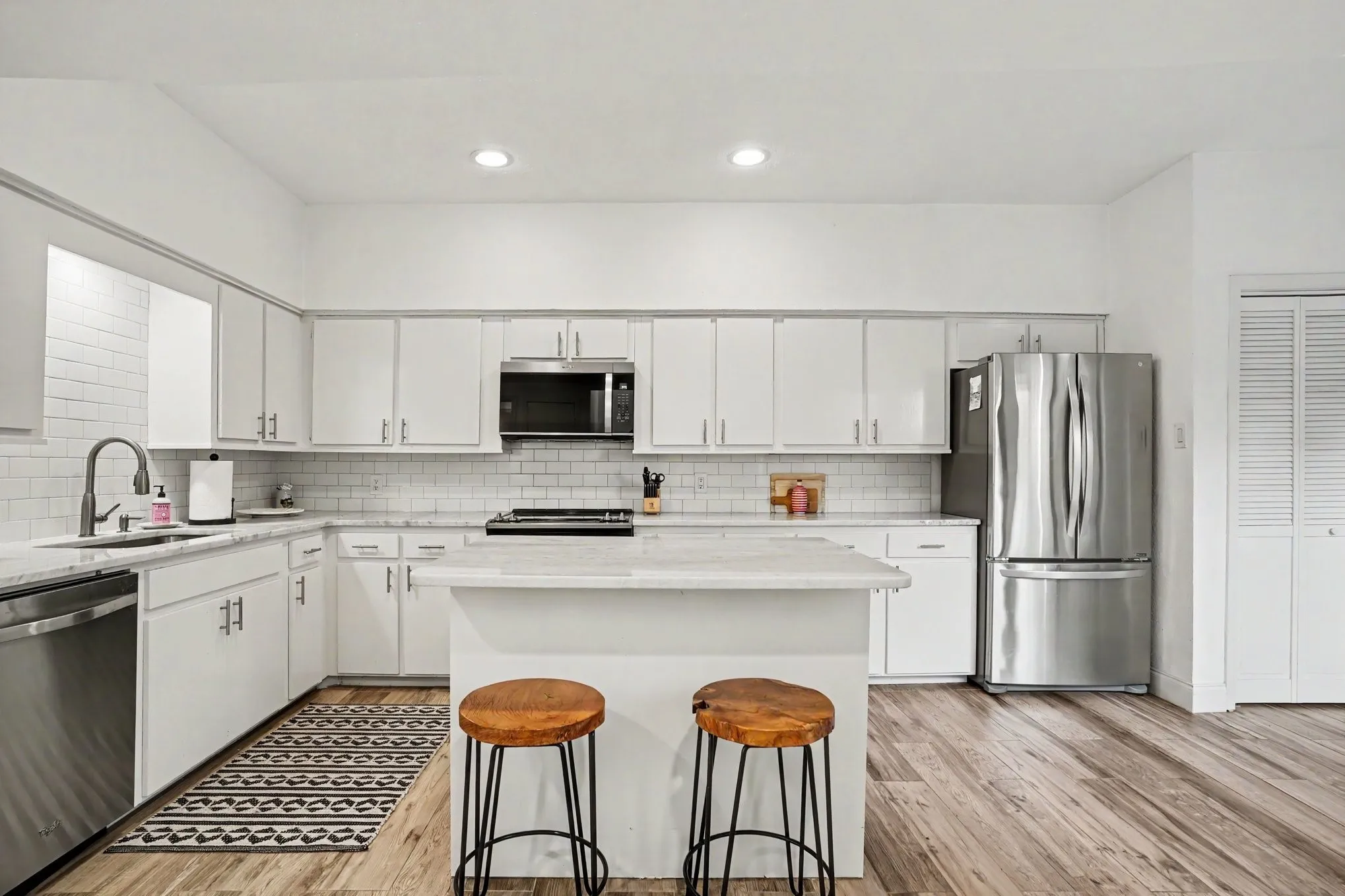 Kitchen featuring an island, white cabinetry, stainless steel appliances, a subway tile backsplash, and wood-finish flooring