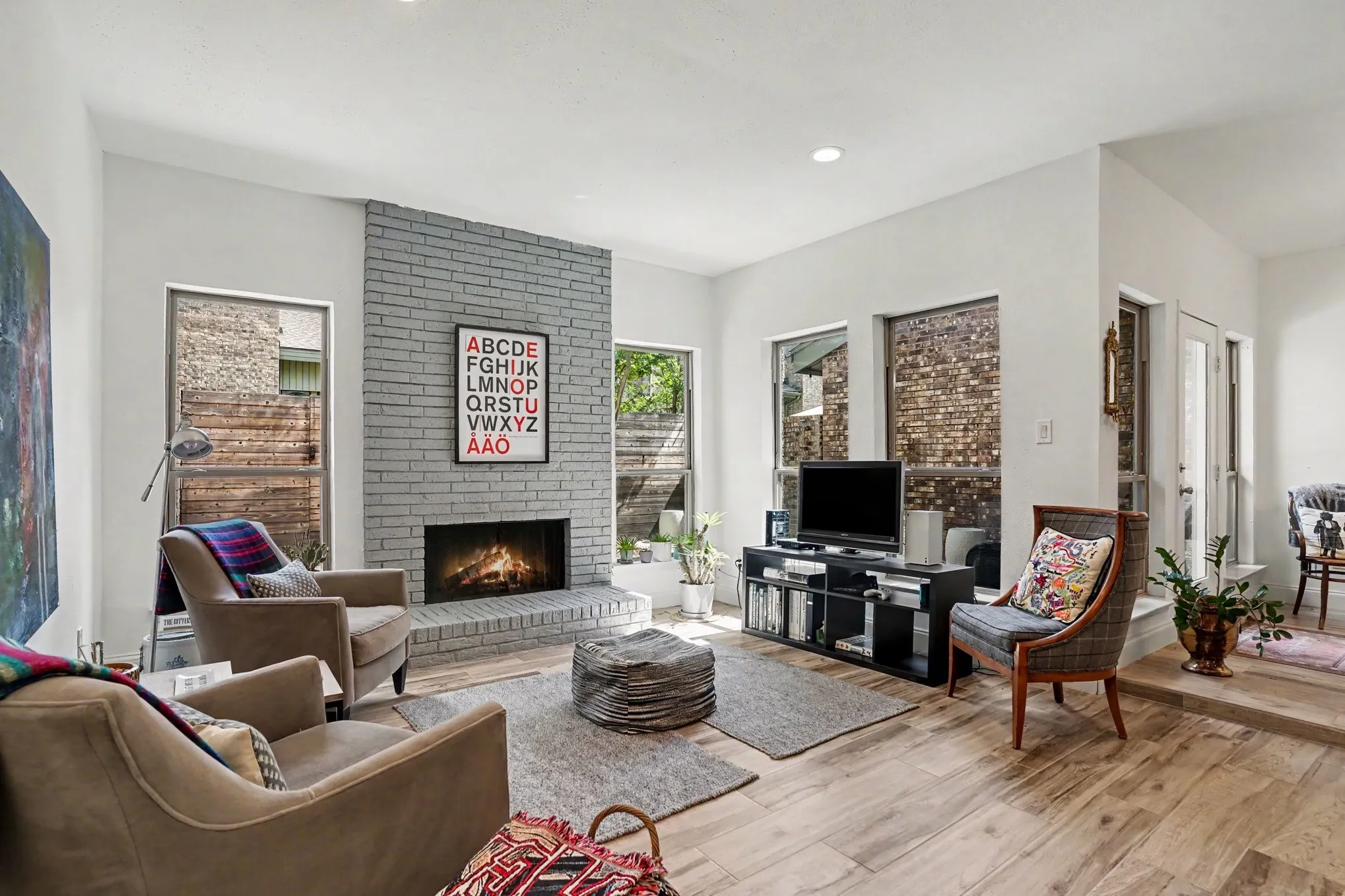 Living area featuring a painted brick fireplace, wood-finish flooring, recessed lighting, and multiple windows