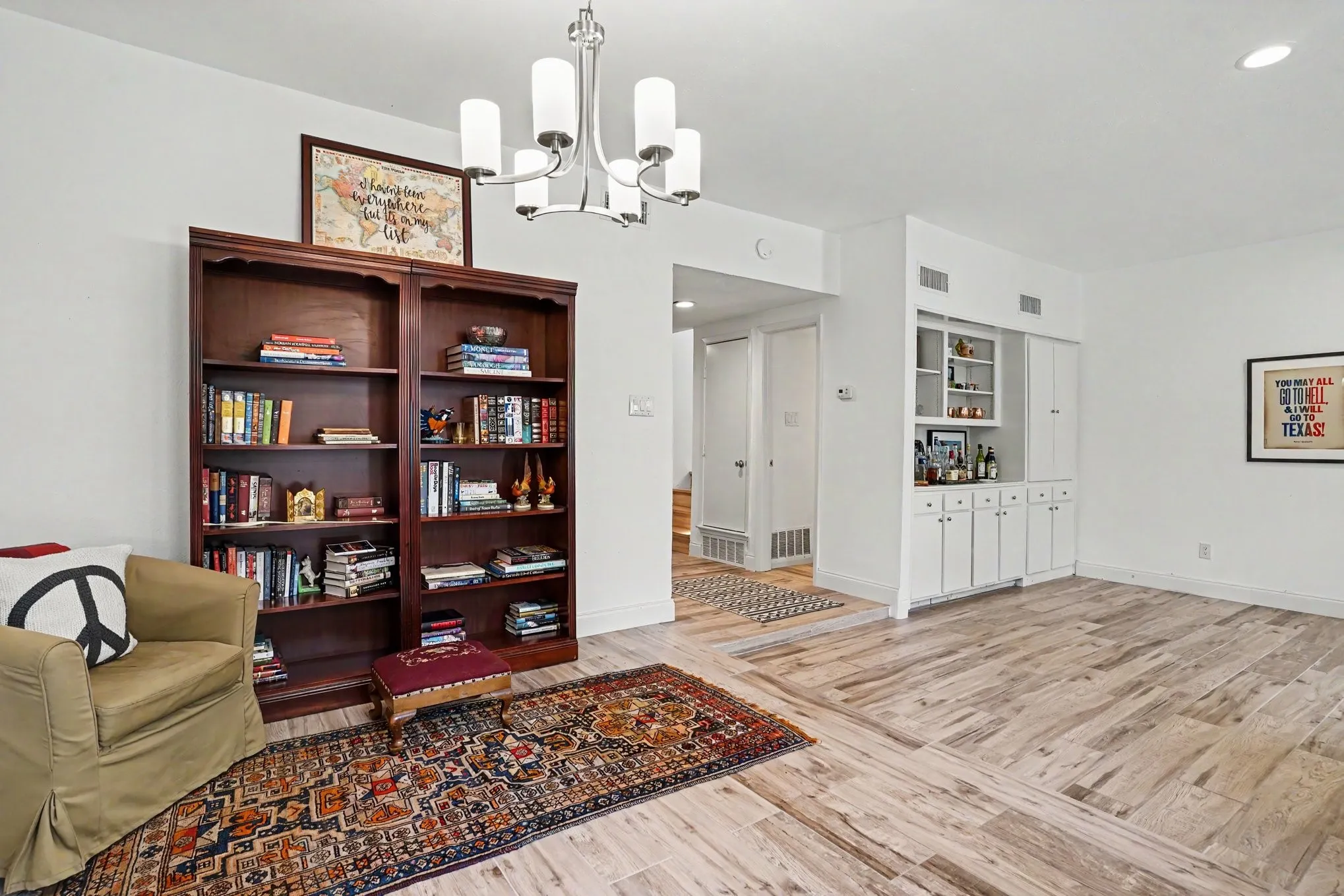 Expansive living area featuring wood-finish flooring, a built-in wet bar with white cabinetry, a built-in shelving unit, a contemporary chandelier, and recessed lighting