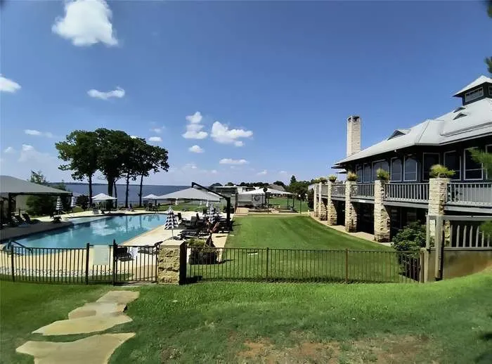 Lakeside property featuring a large swimming pool, expansive lawn, and a multi-level structure with an upper balcony