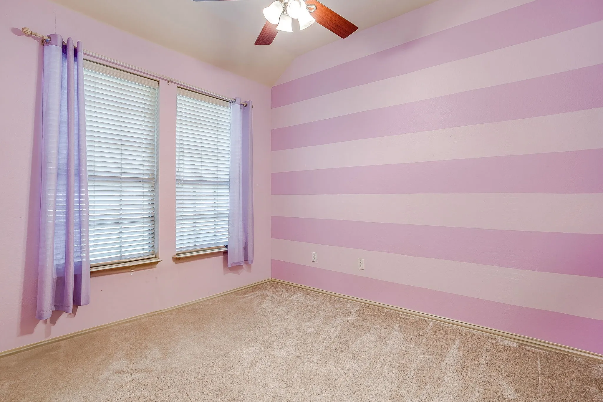 Vaulted ceiling featuring a ceiling fan with integrated lighting, two windows with blinds, and carpeted flooring