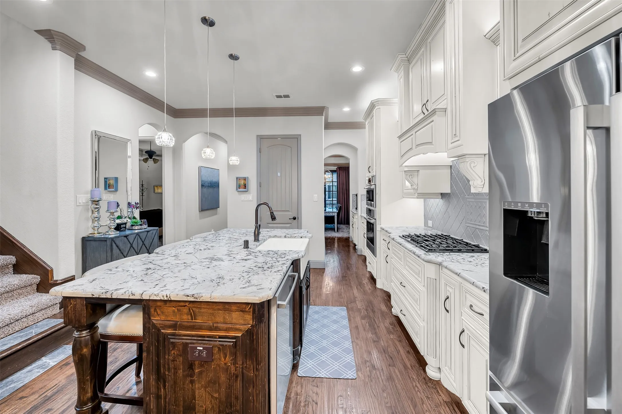 Gourmet kitchen featuring a large island with a farmhouse sink, stainless steel appliances, white cabinetry, and wood-finish flooring