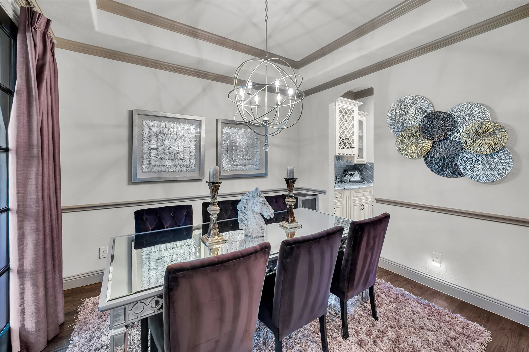 Elegant dining space featuring tray ceilings with crown molding, wood-finish flooring, and a contemporary chandelier