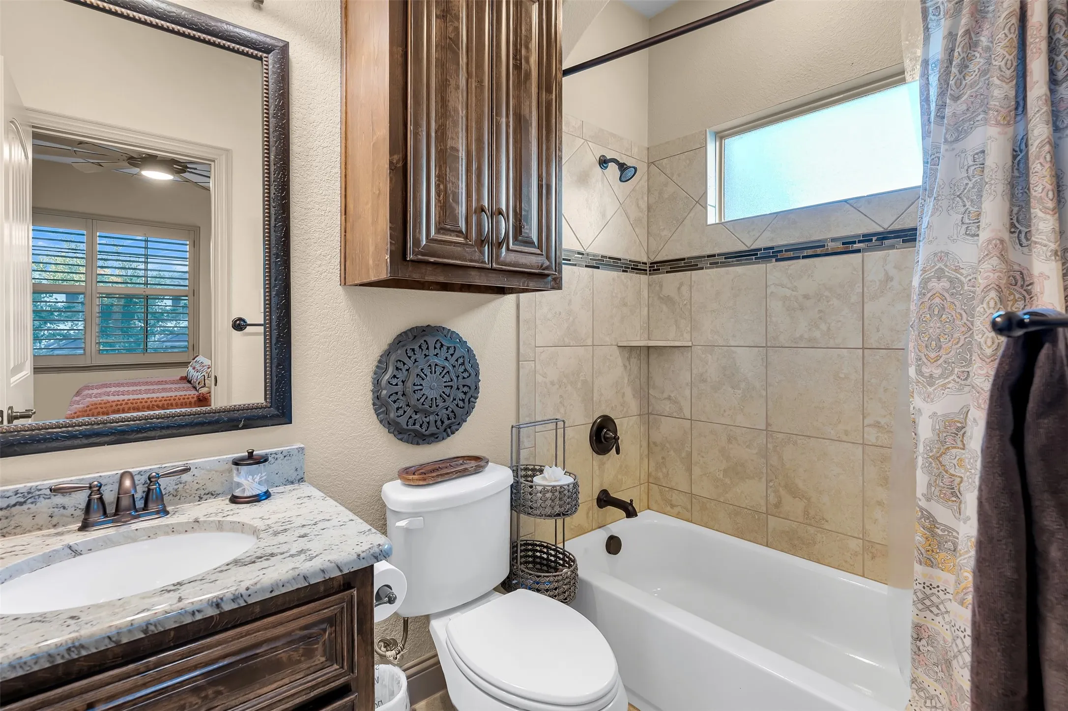 Bathroom featuring a white bathtub, tiled shower surround with accent band, single vanity with light-toned countertop, and dark wood-finish cabinetry