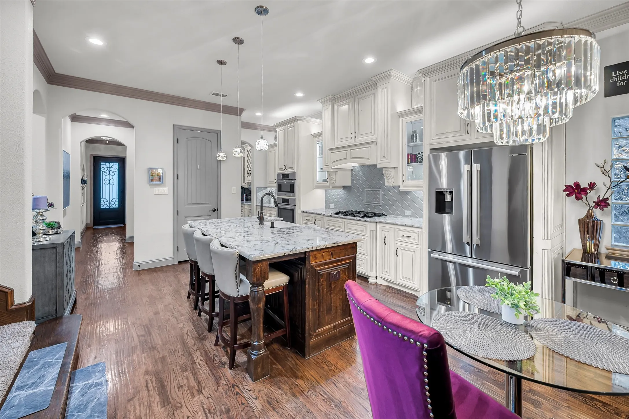 Gourmet kitchen featuring a large island with seating, pendant lighting, stainless steel appliances, and white cabinetry