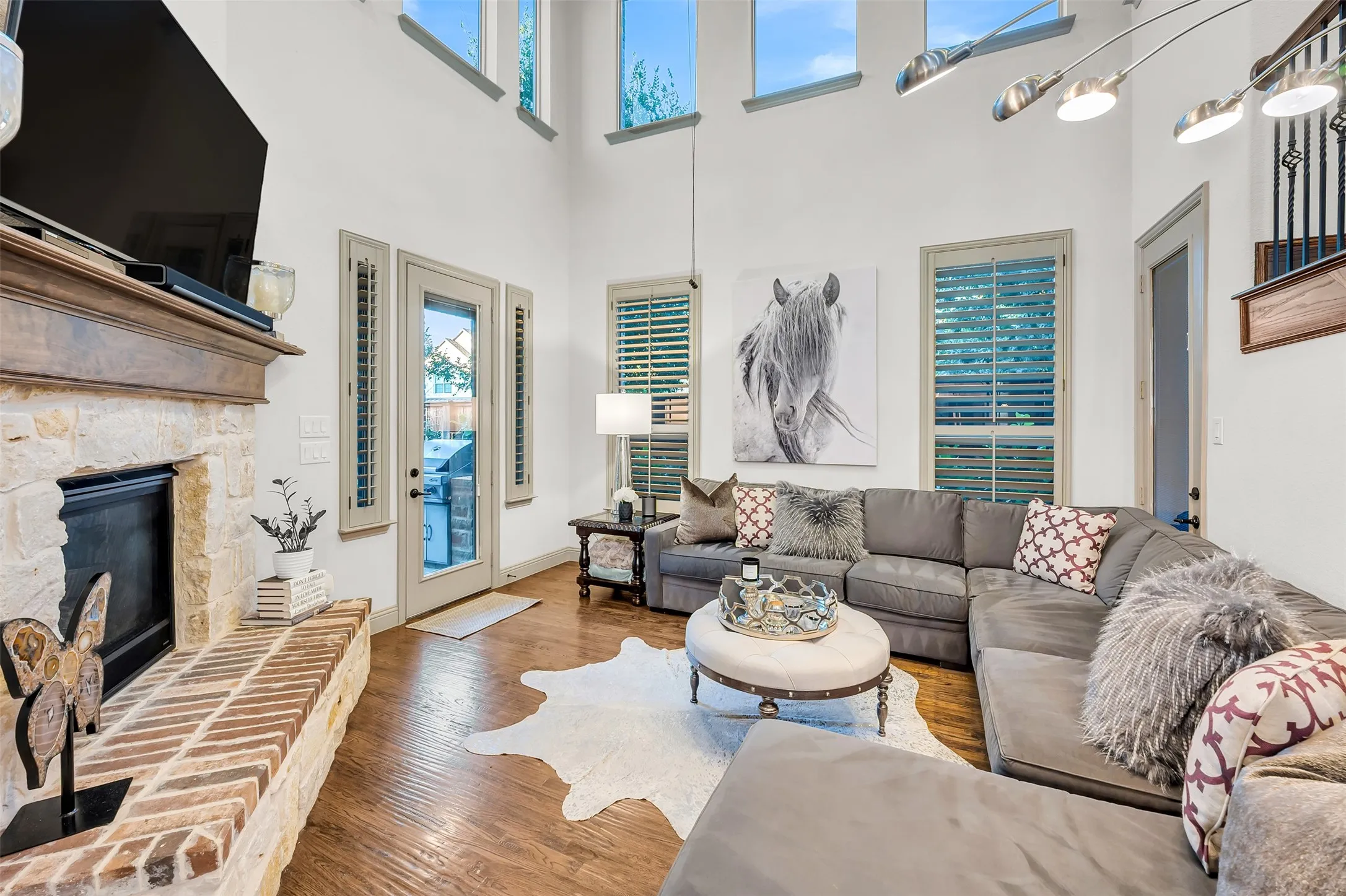 Living area featuring high ceilings with upper-level windows, wood-finish flooring, and a stone fireplace with a brick hearth