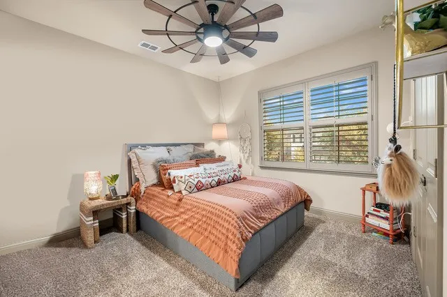 Carpeted interior with a ceiling fan, window with plantation shutters, and a built-in closet system