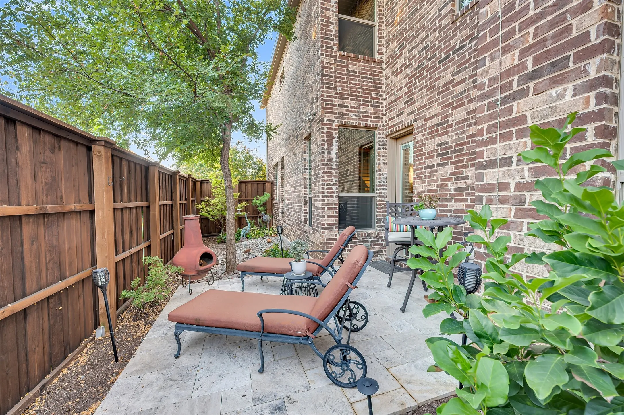 Private patio space featuring light-toned paver flooring and a dark wood fence