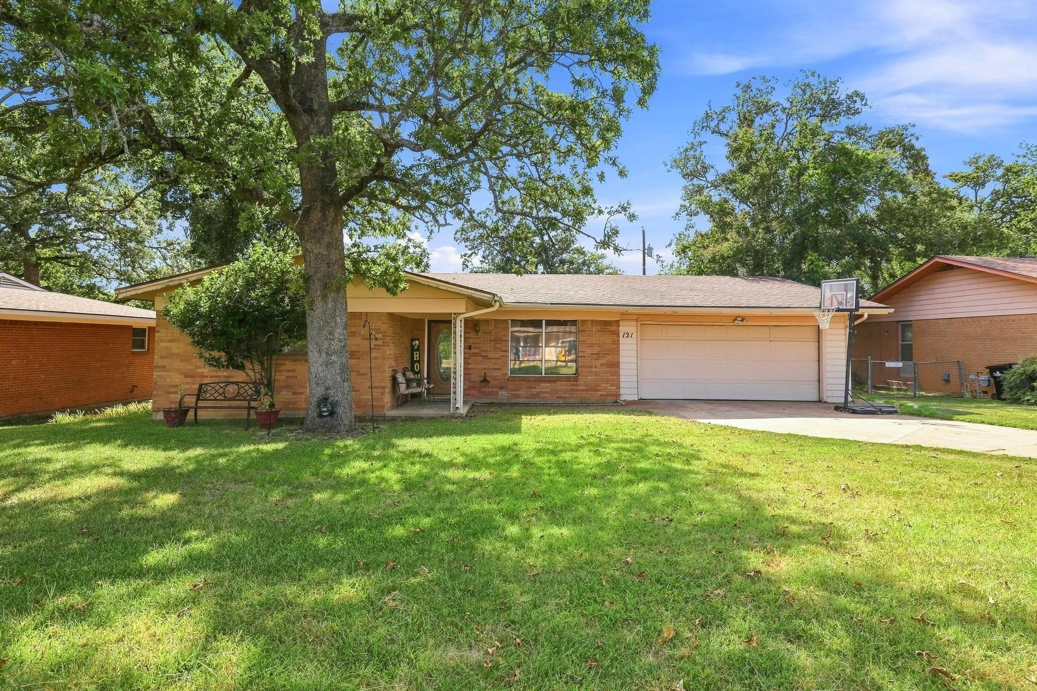 Brick exterior, attached garage, covered front entry, mature trees, and a concrete driveway