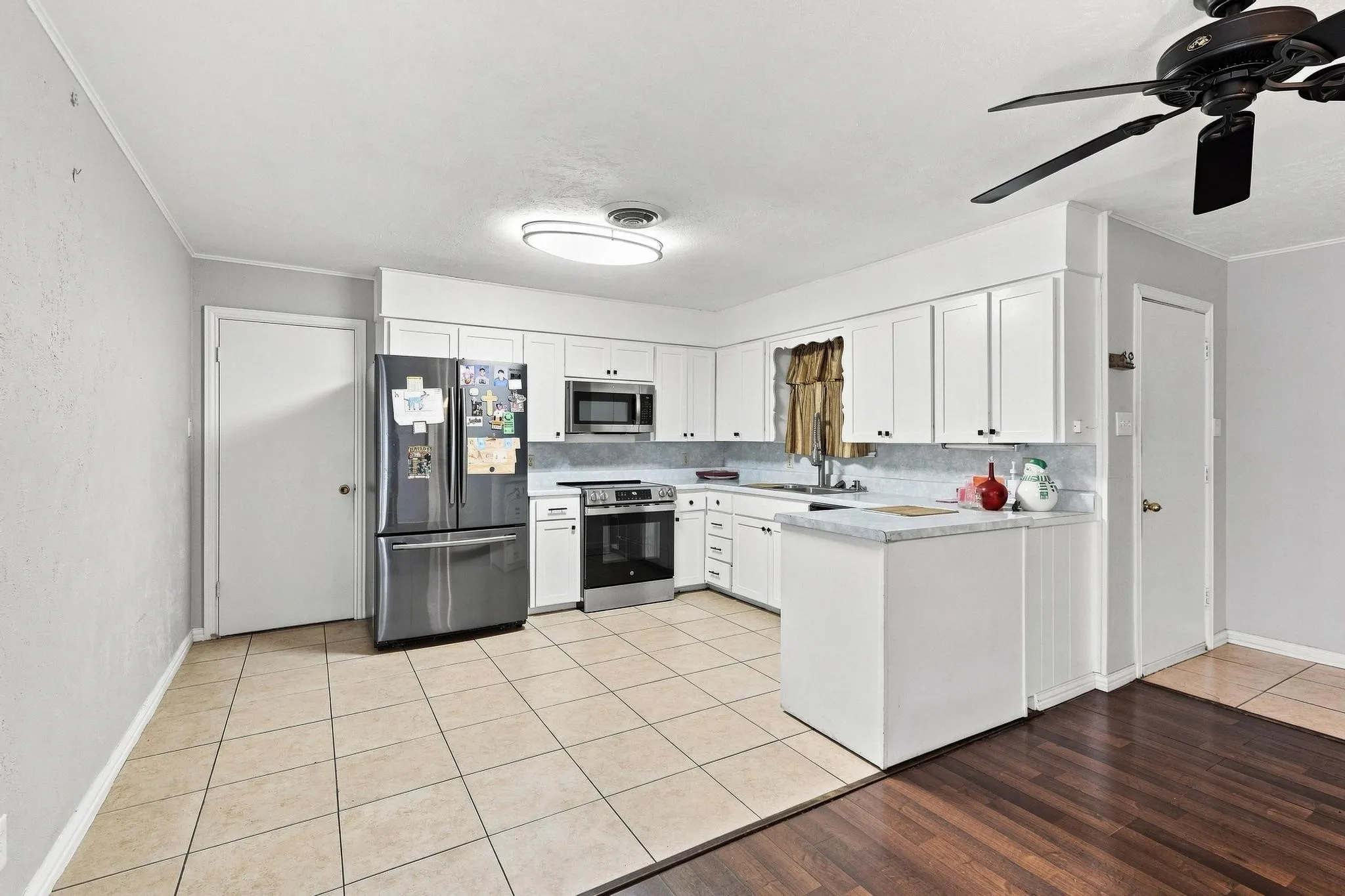 White cabinetry with dark hardware, stainless steel appliances, tile flooring, and a ceiling fan