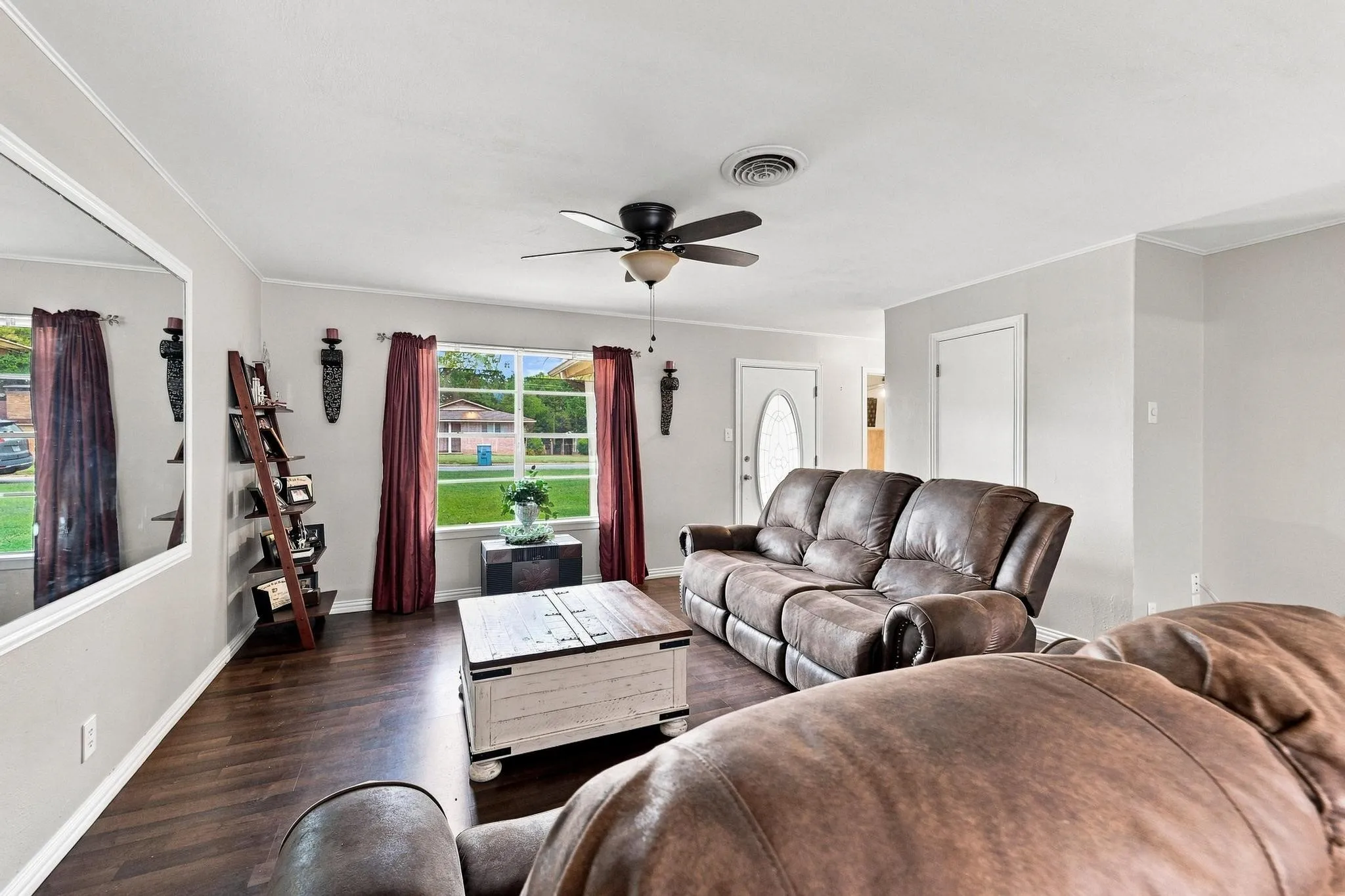 Wood-finish flooring, ceiling fan with light fixture, multiple windows, and a white paneled door
