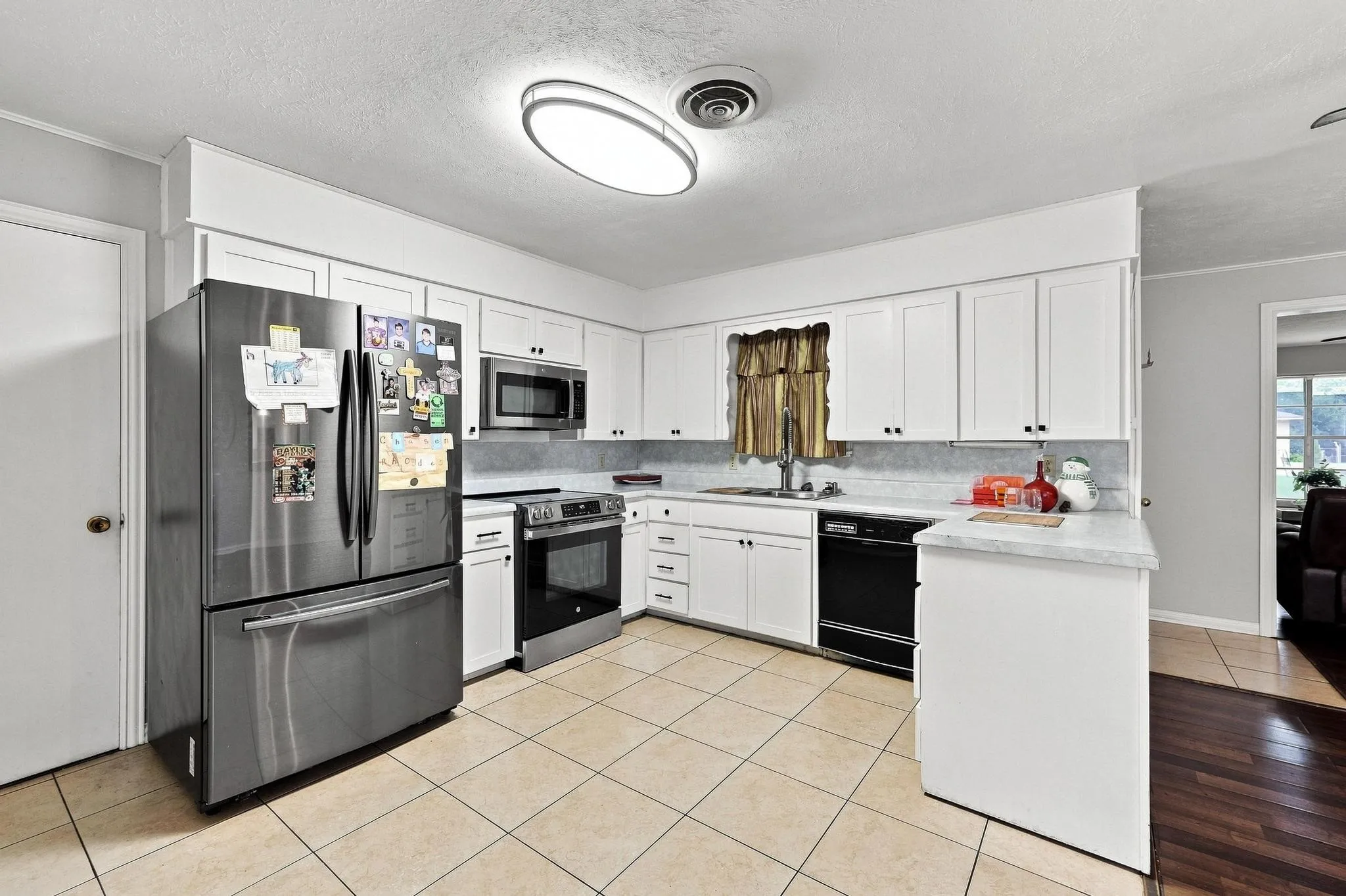 White cabinetry with black hardware, stainless steel appliances, light-toned tile flooring, and white countertops