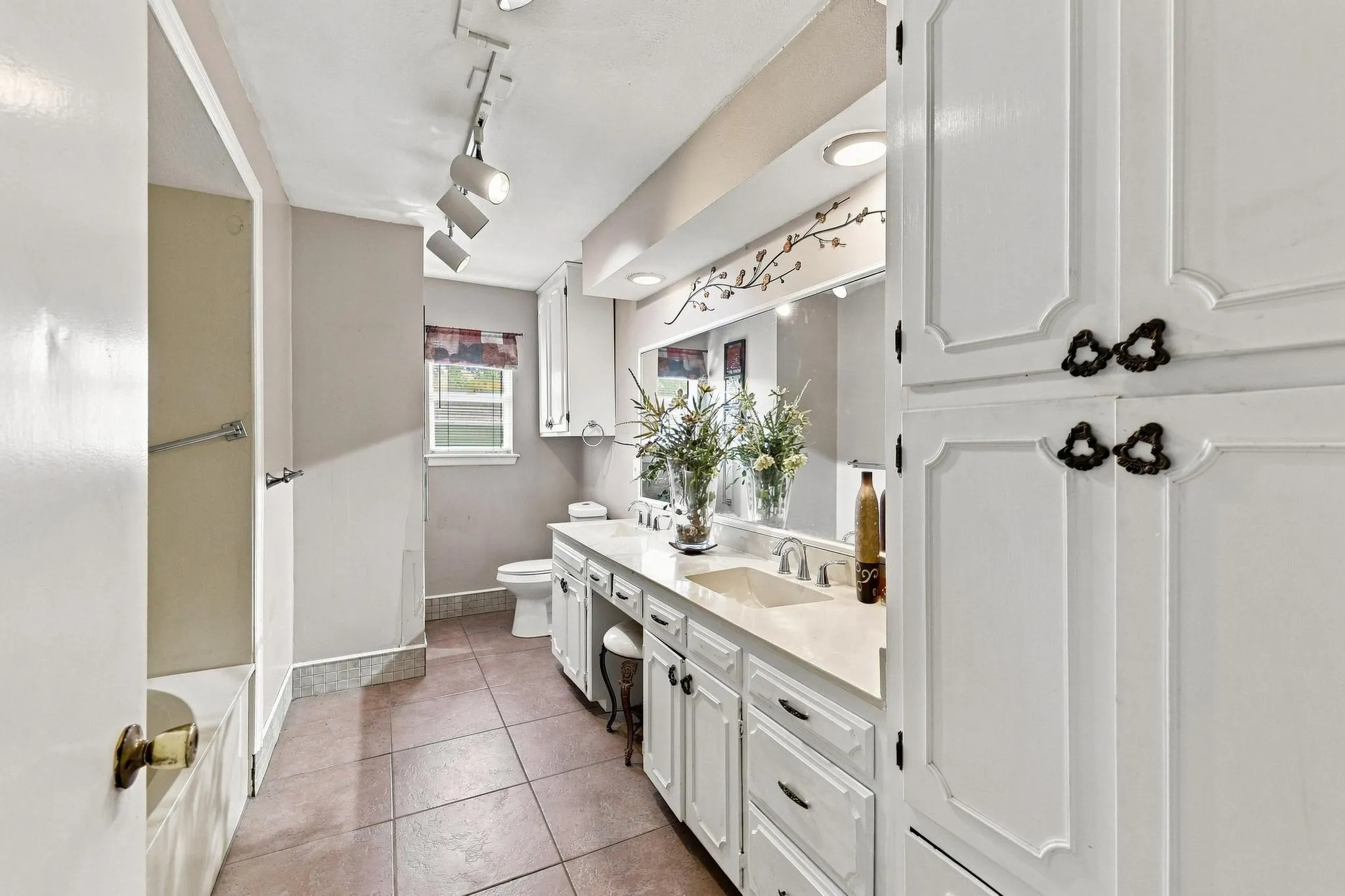 Built-in storage cabinetry, track lighting, vanity with integrated sink, stone countertop, and tile flooring