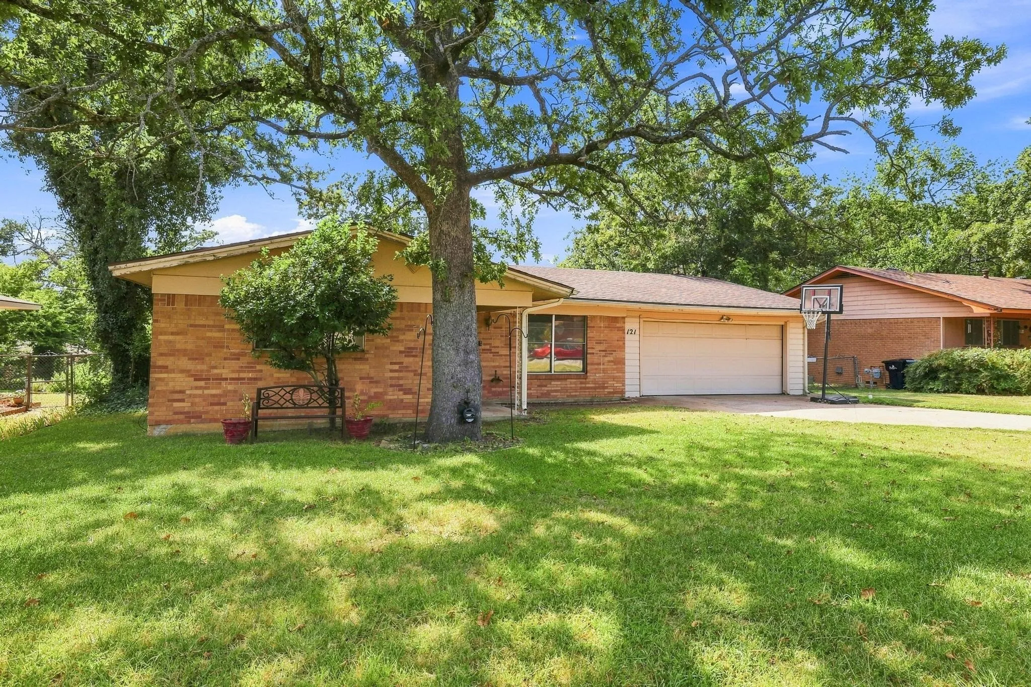 Brick exterior with an attached garage, featuring a mature shade tree and established landscaping