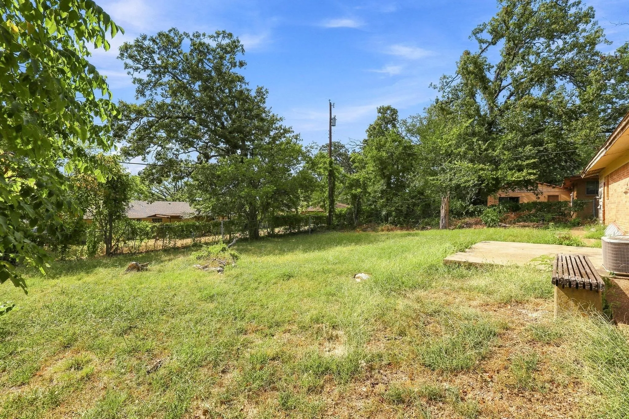 Expansive grassy yard with mature trees and a concrete patio