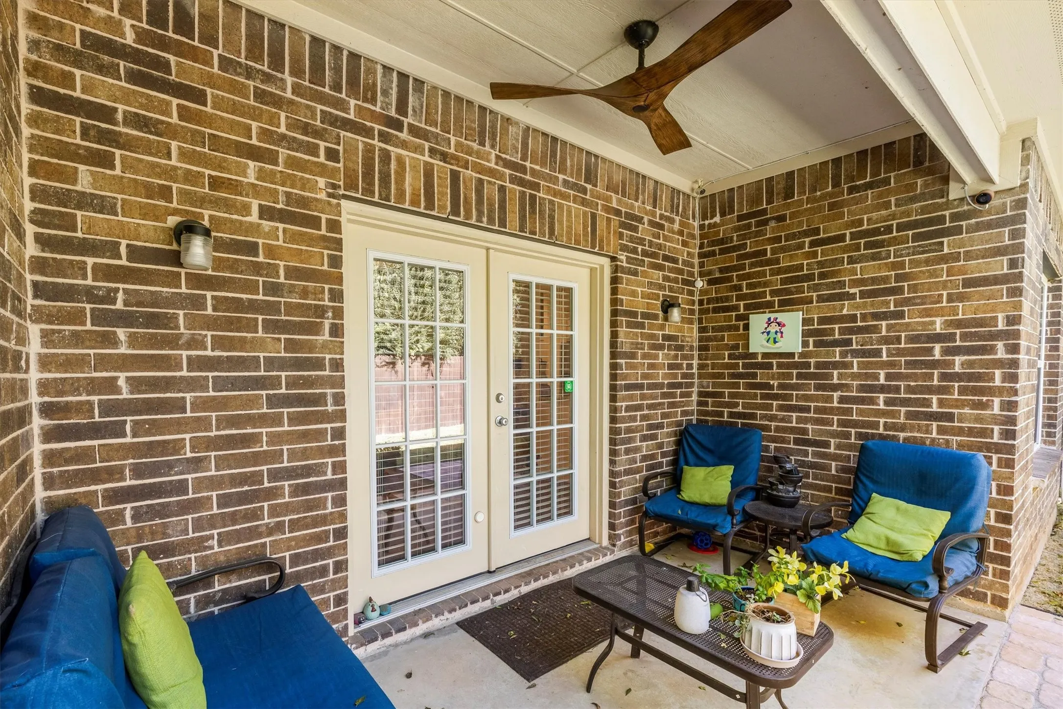 Covered patio featuring a ceiling fan, brick exterior, and outdoor lighting fixtures