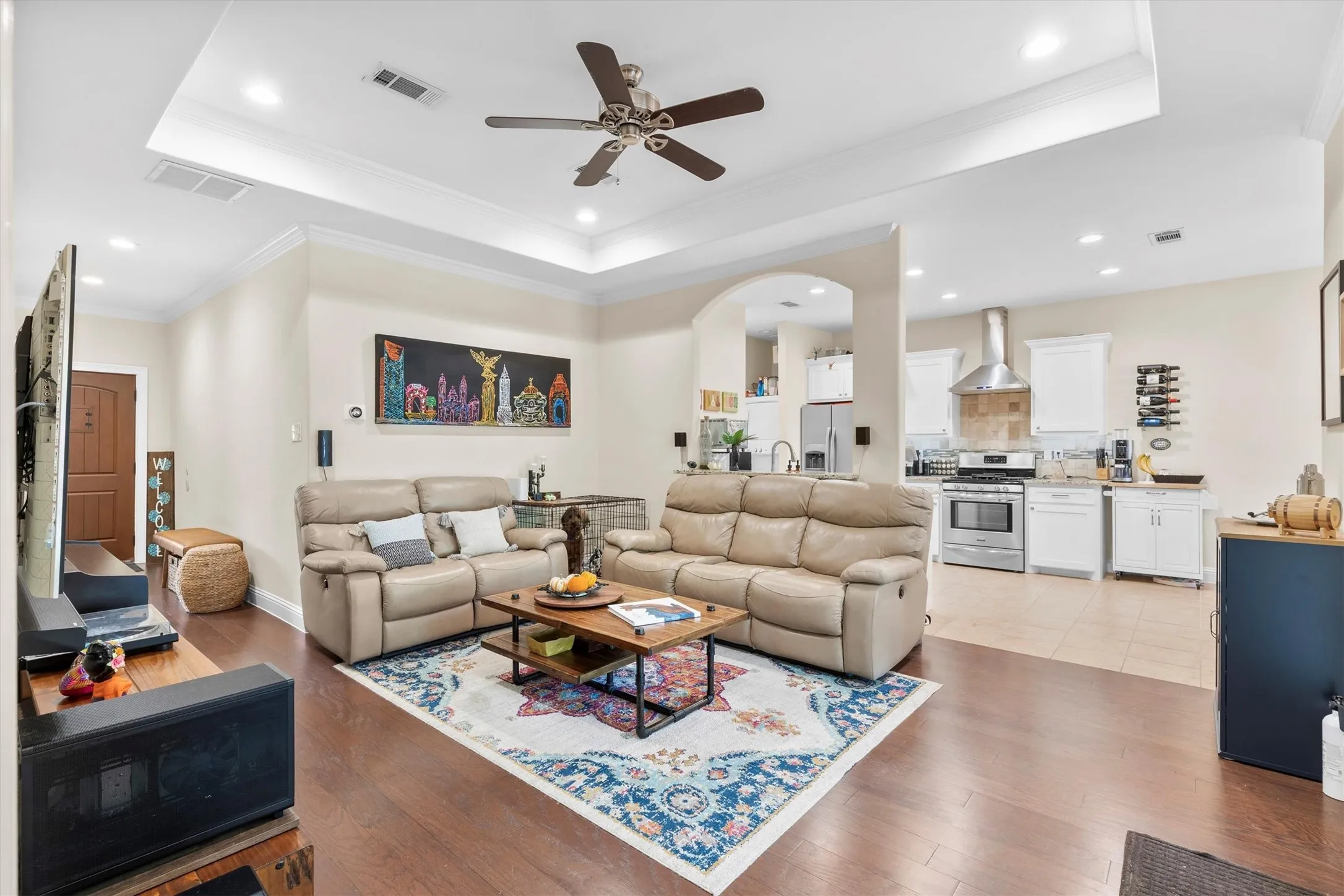Spacious open-concept living area featuring wood-finish flooring and a tray ceiling with a ceiling fan