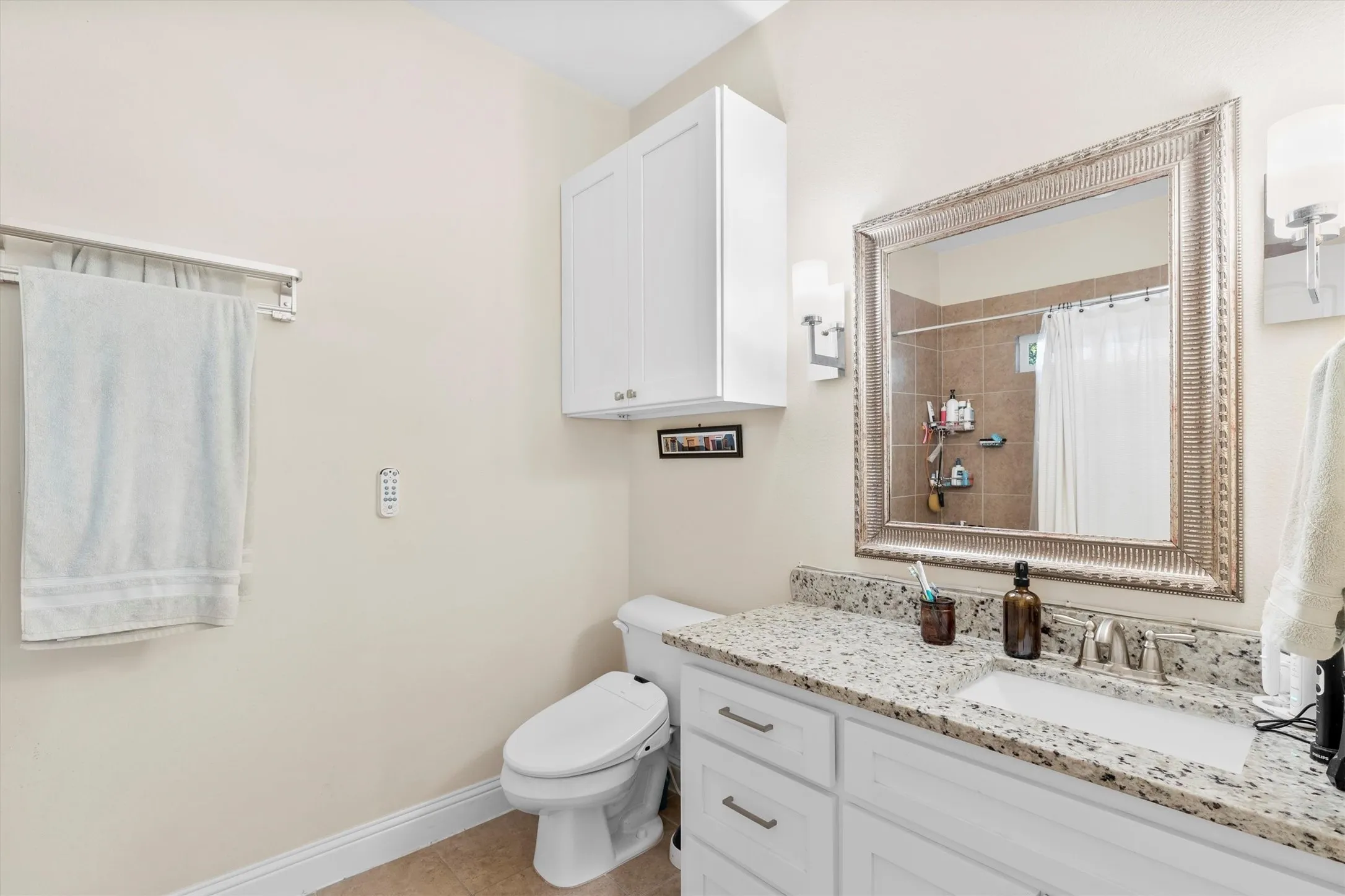 Bathroom vanity featuring a speckled countertop, white cabinetry with silver hardware, and an ornate framed mirror