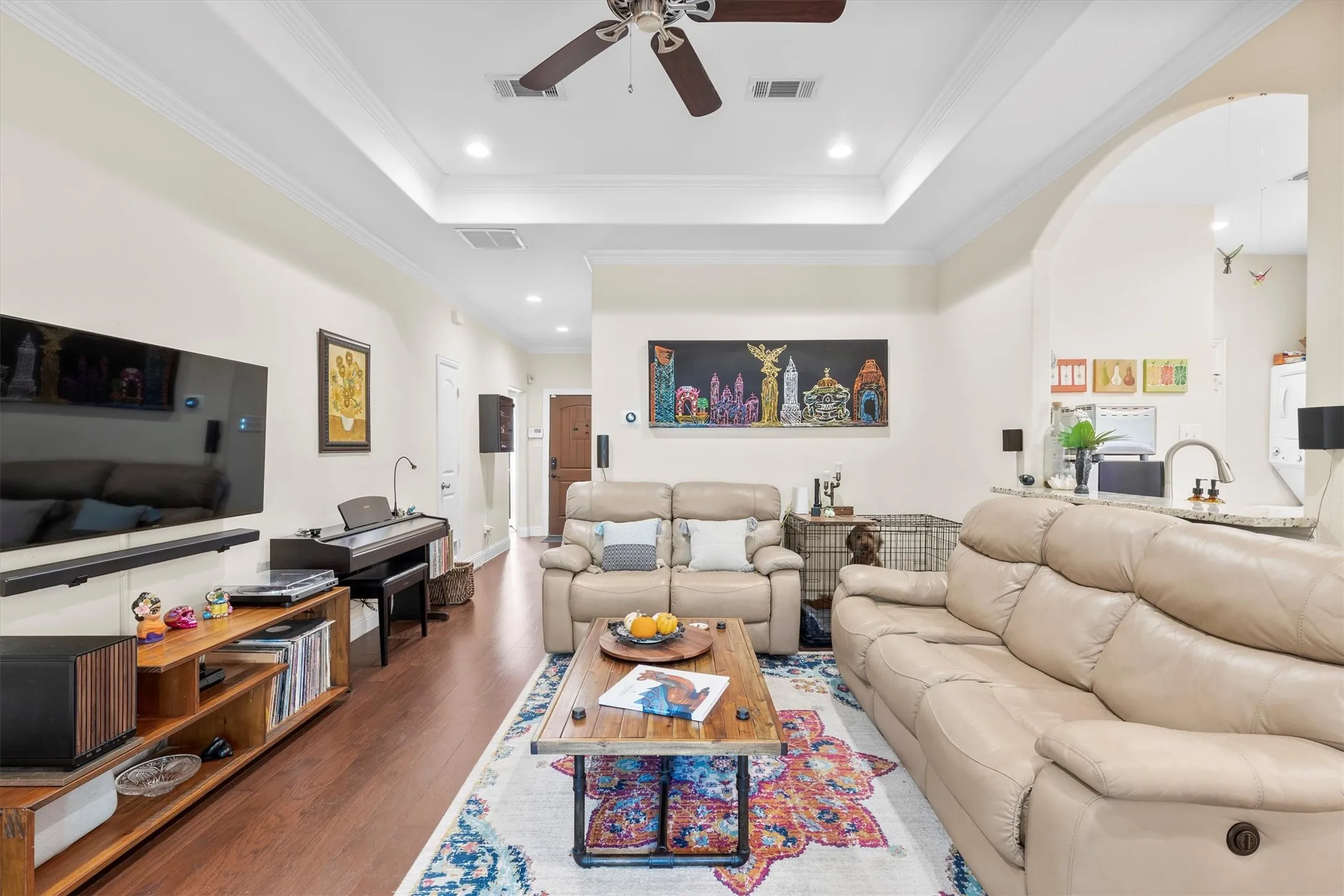 Spacious living area featuring wood-finish flooring, a tray ceiling with recessed lighting, and crown molding