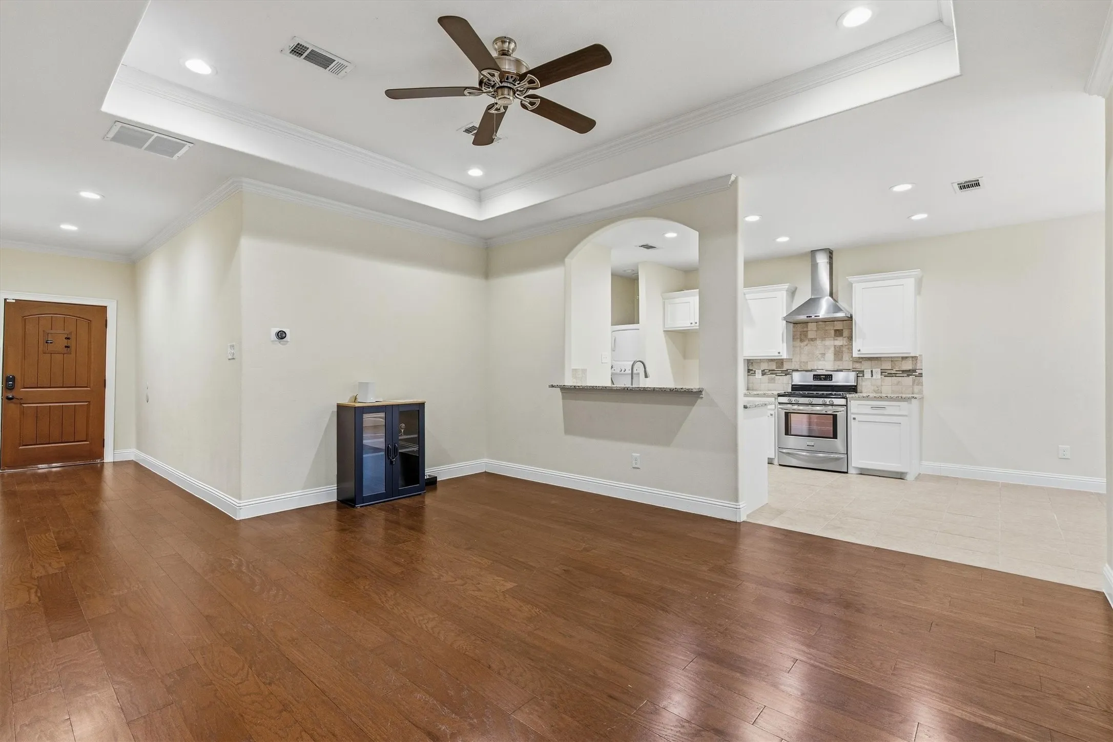 Rich wood-finish flooring, tray ceiling with recessed lighting, carved wood entry door, kitchen with stainless steel range and range hood, and breakfast bar