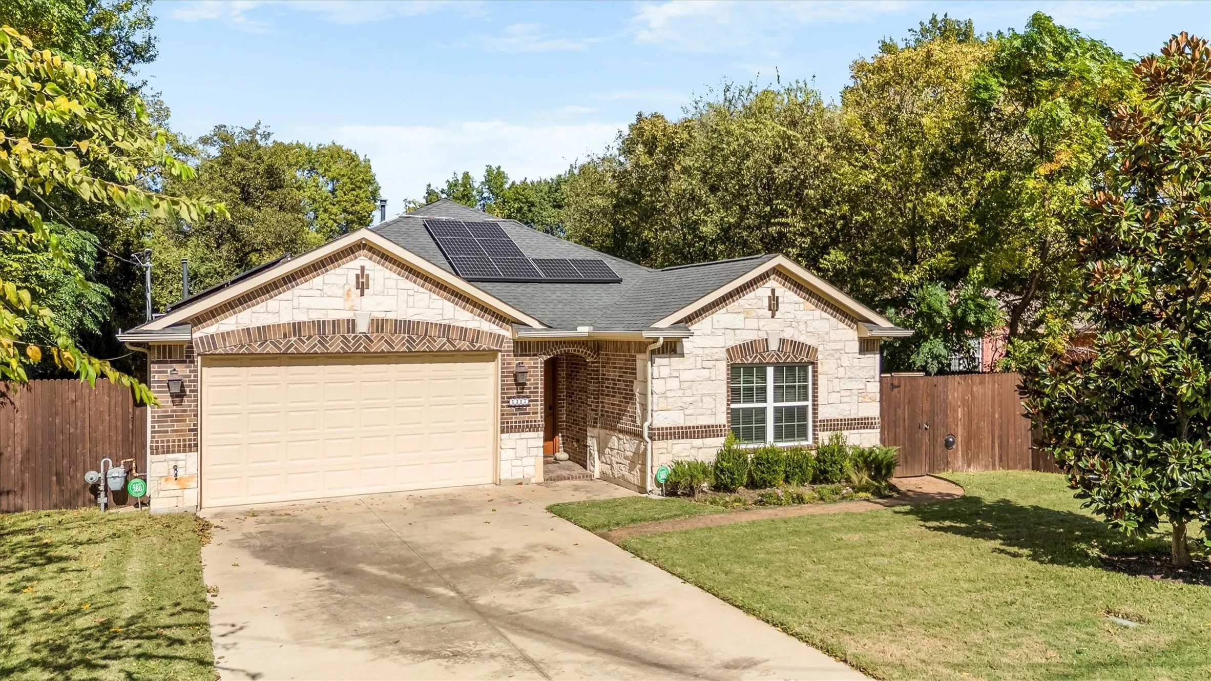 Stone and brick facade home featuring a two-car garage, solar panels, and mature landscaping