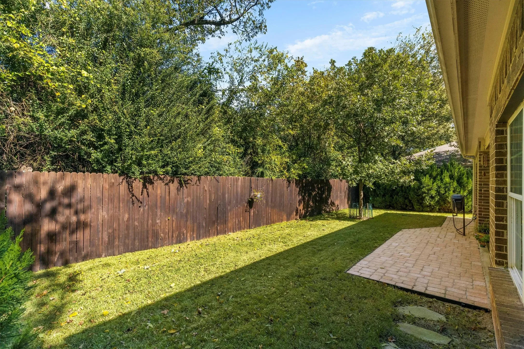 Private backyard featuring a paver patio and stepping stones, surrounded by a wood fence and mature trees