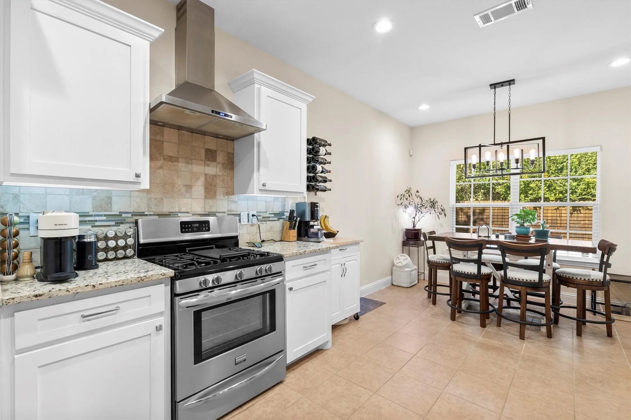 Kitchen and dining area featuring white cabinetry, stainless steel appliances, granite-style countertops, mosaic tile backsplash, and recessed lighting