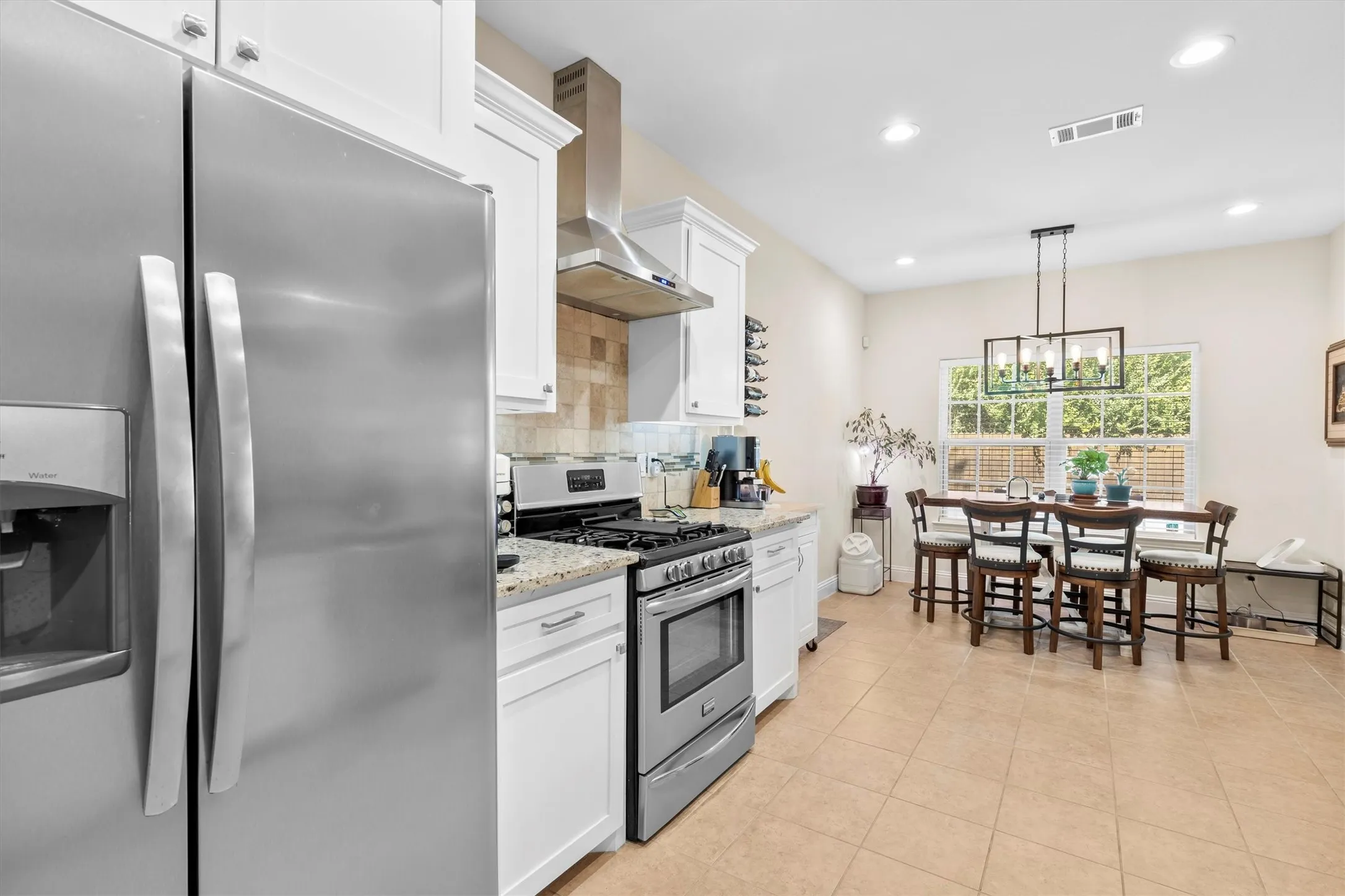 Kitchen and dining area featuring stainless steel appliances, white cabinetry, granite countertops, and tiled flooring