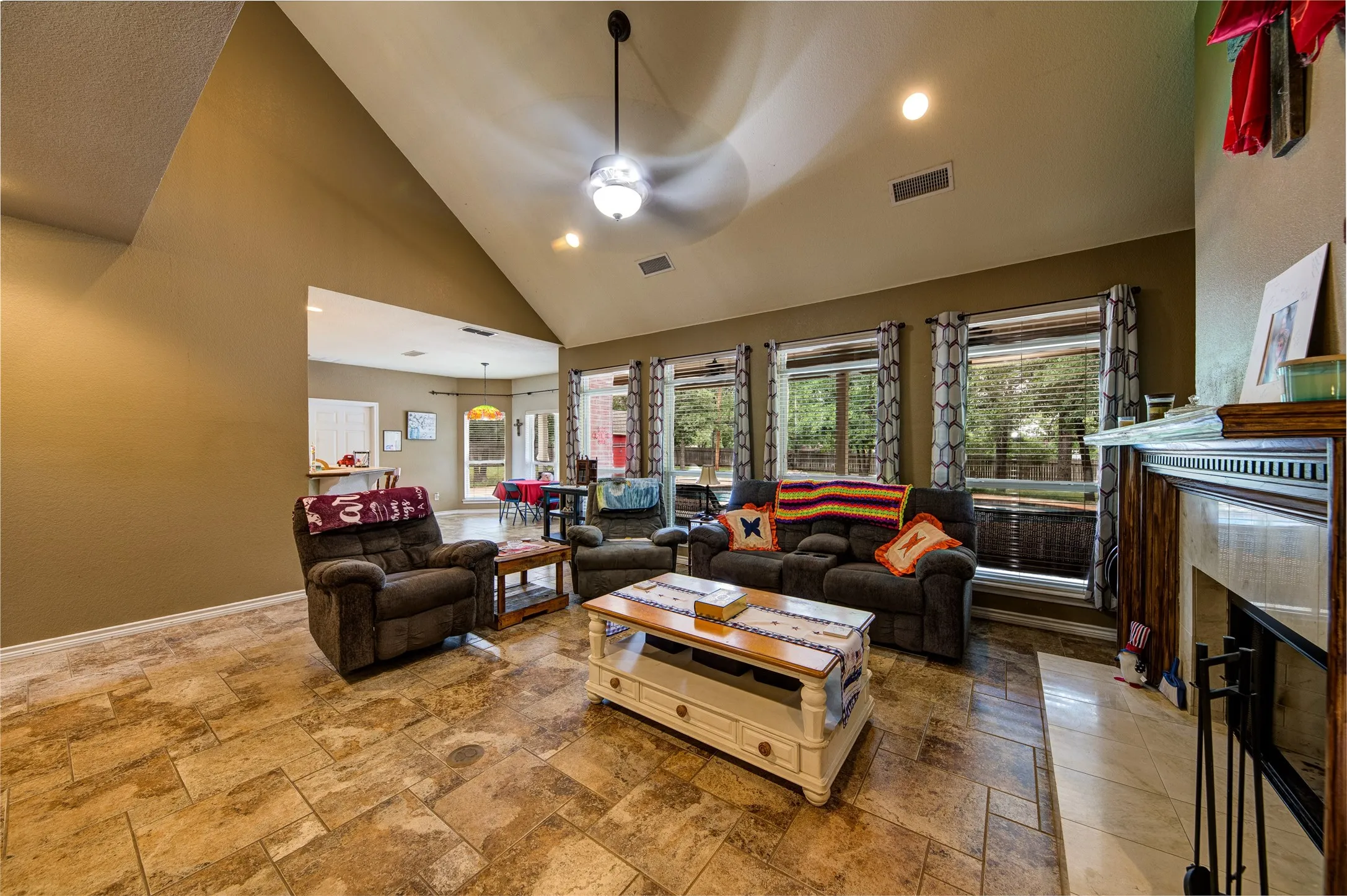 Spacious living area featuring a vaulted ceiling with a ceiling fan, recessed lighting, and large windows with blinds