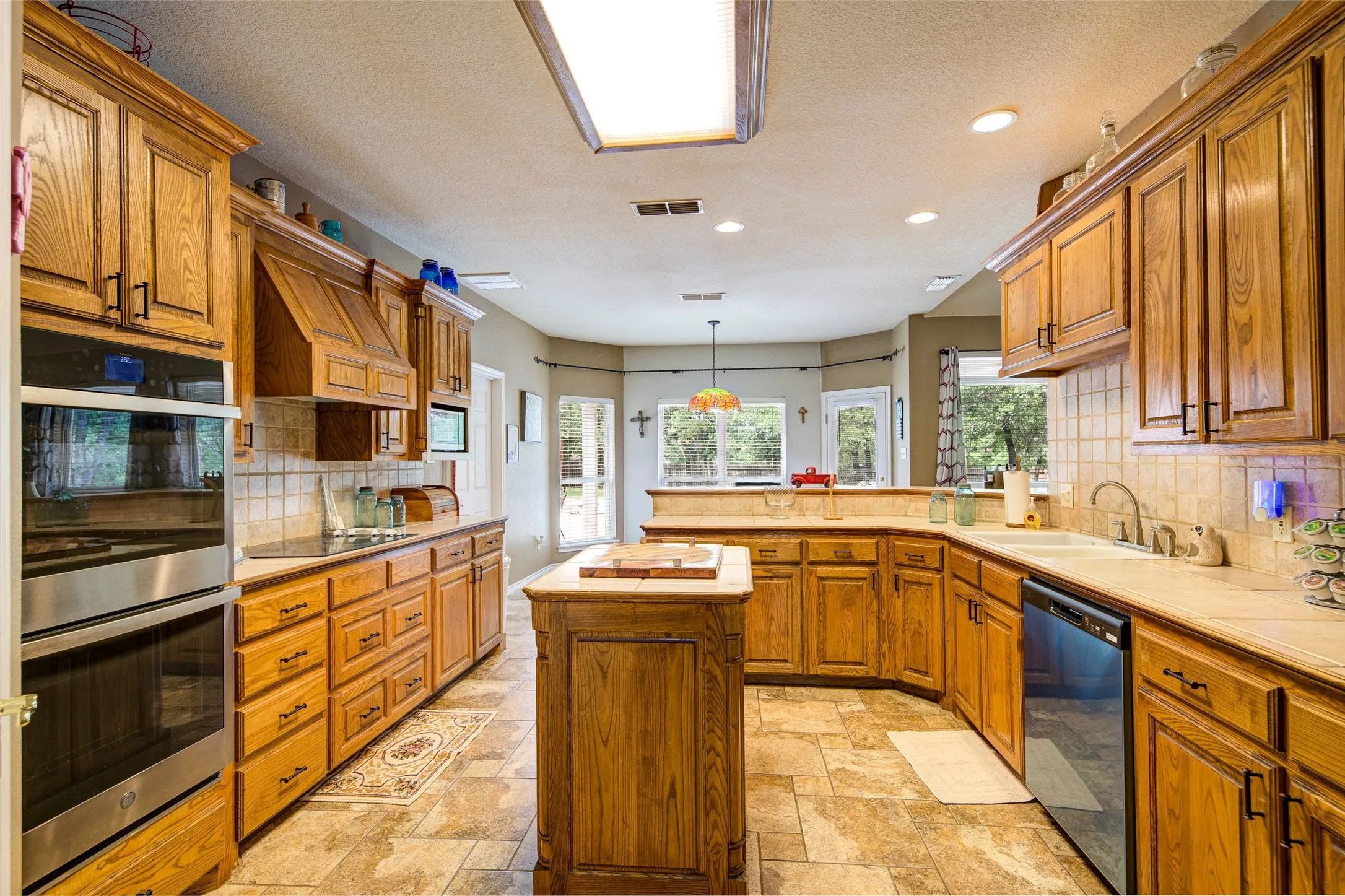 Spacious kitchen featuring extensive wood cabinetry, tile flooring, recessed lighting, a stainless steel double oven, and a central wood island