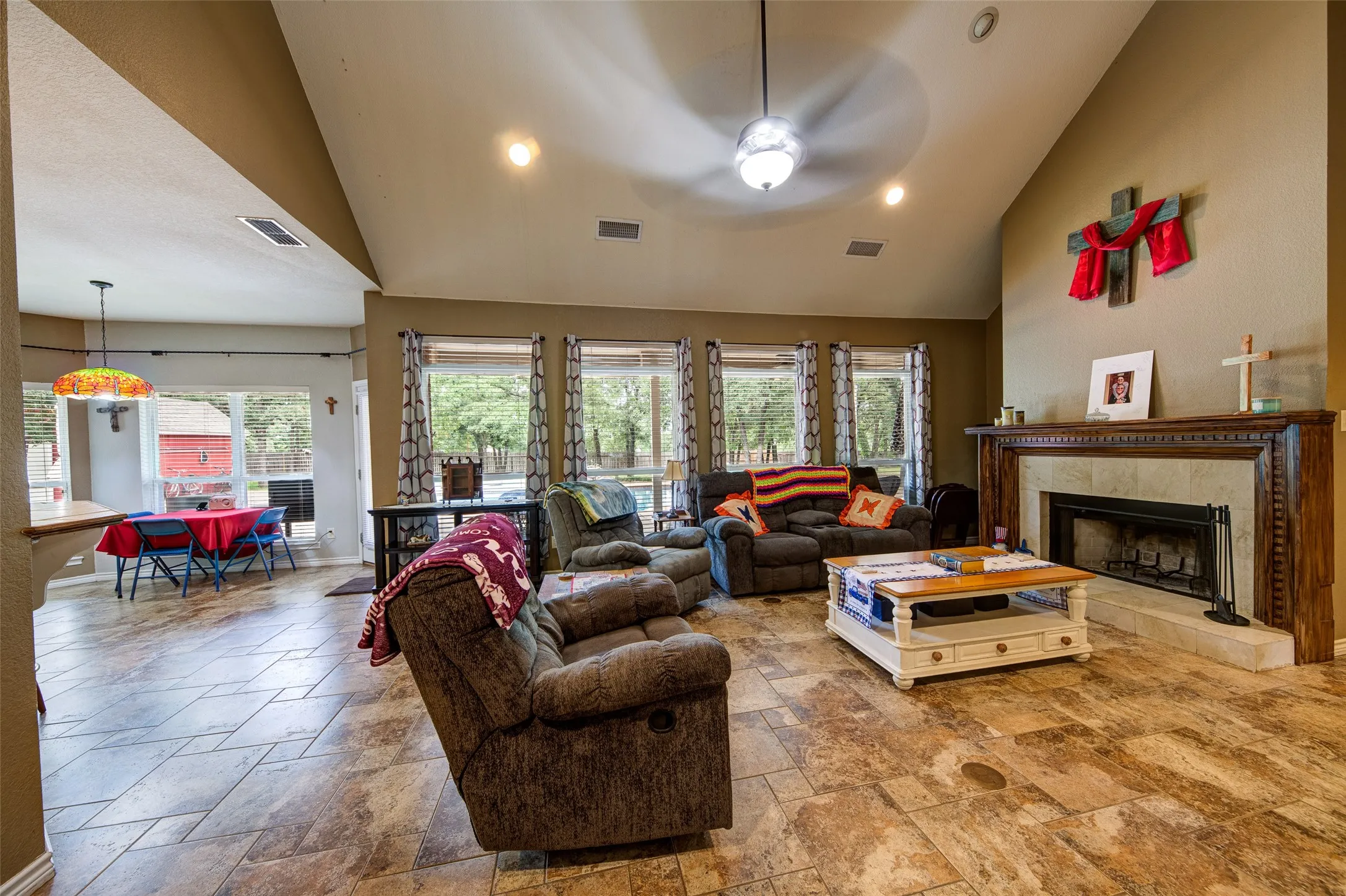 Vaulted ceiling living area featuring a stone-surround fireplace with a wood mantle, tile flooring, and multiple windows